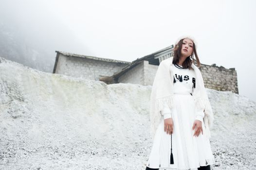 Stylish woman in winter attire standing in snowy mountainous landscape.