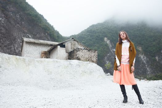 A stylish woman in a skirt standing in a rocky, foggy mountainous area.