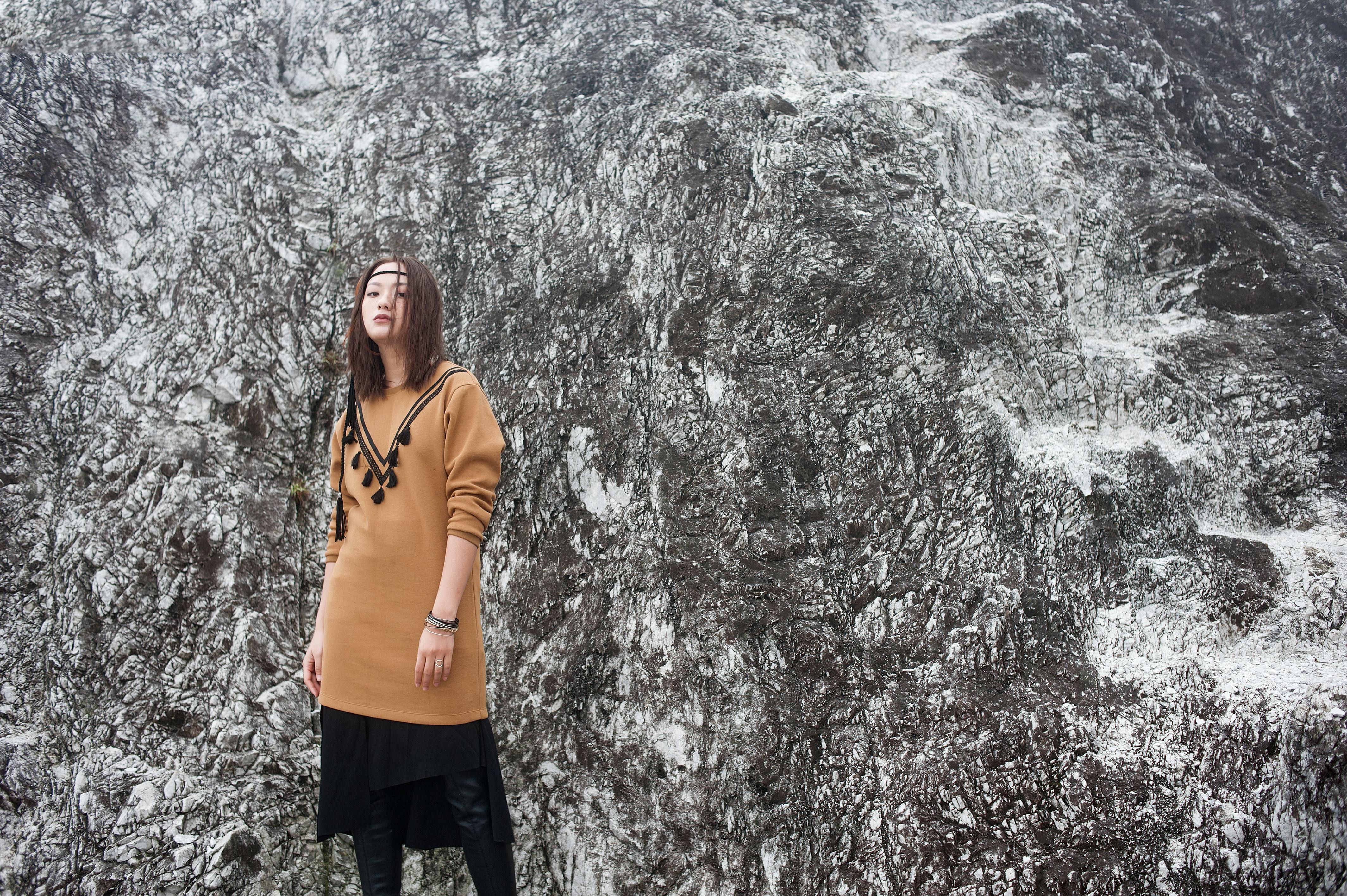 ingyenes Divatos öltözékű nő ​​magabiztosan áll egy texturált sziklás sziklafal mögött. Stockfotó