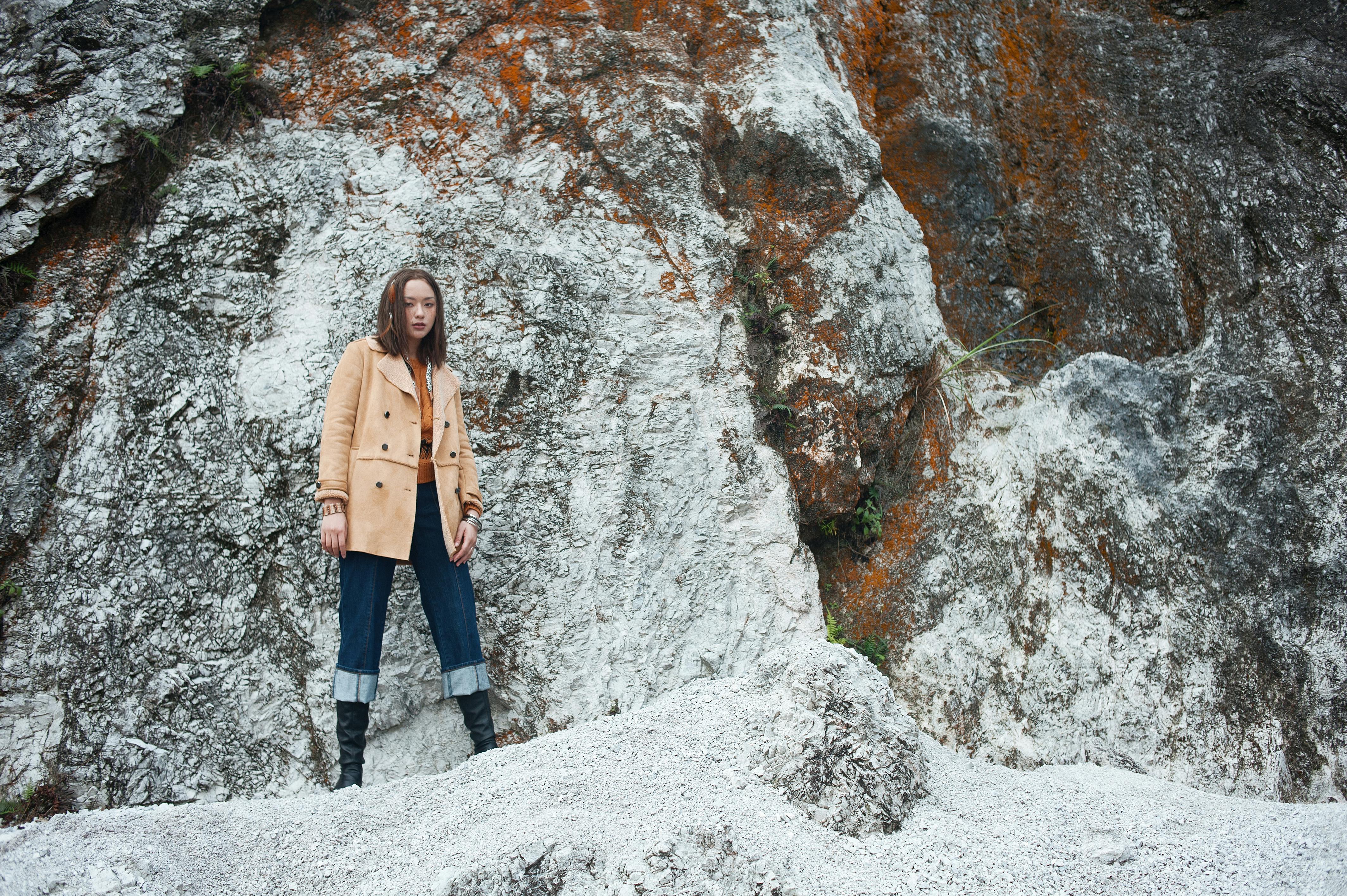 Gratis Kvinne i stilig antrekk står mot en steinvegg og viser frem mote og natur. Arkivbilde
