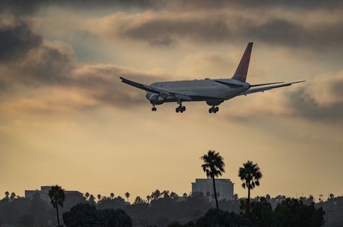 Free Large airliner approaching Los Angeles Airport at sunset, silhouetted against palm trees and dramatic sky. Stock Photo