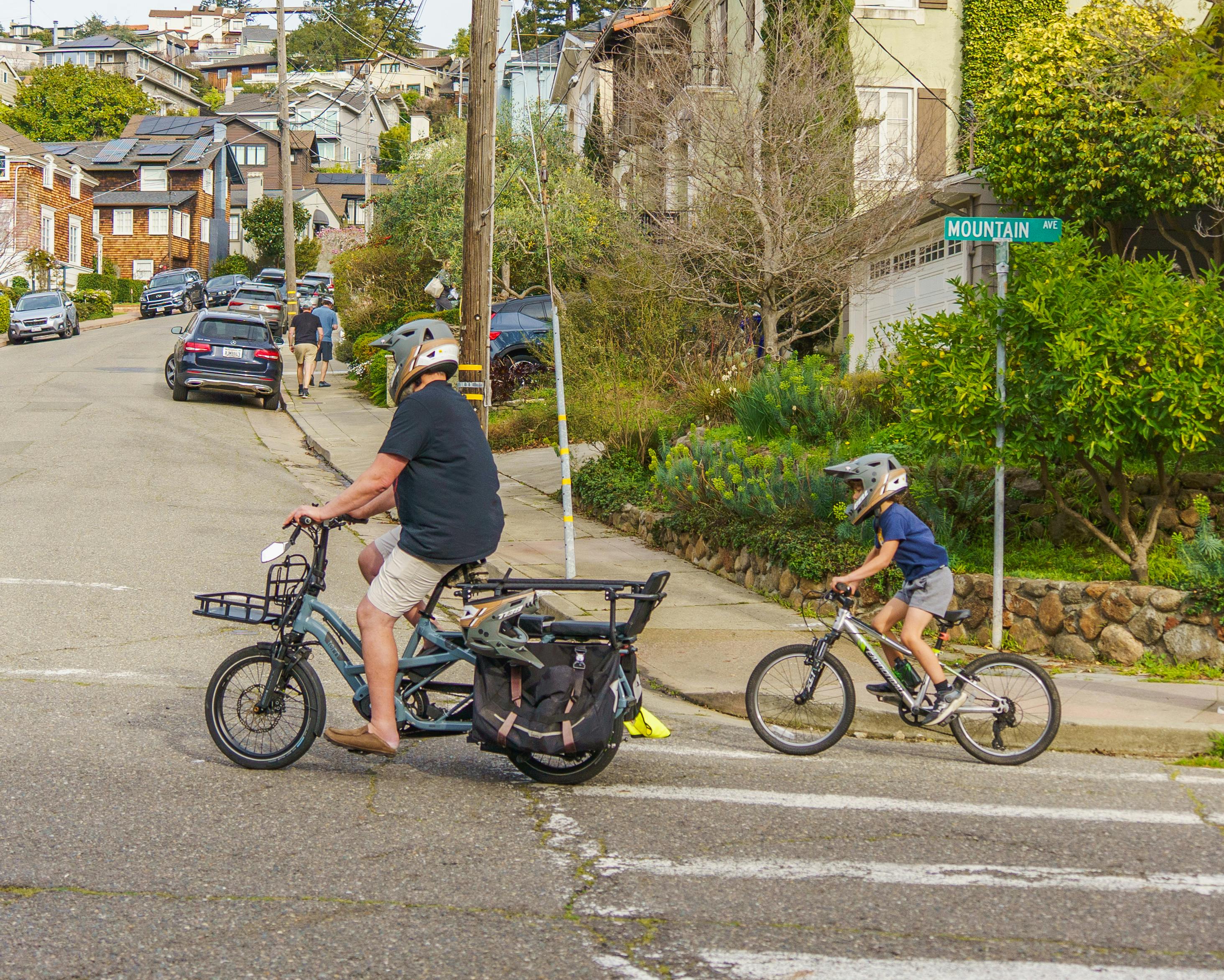 Man and child in helmets cycling through a residential area by Mountain Avenue.