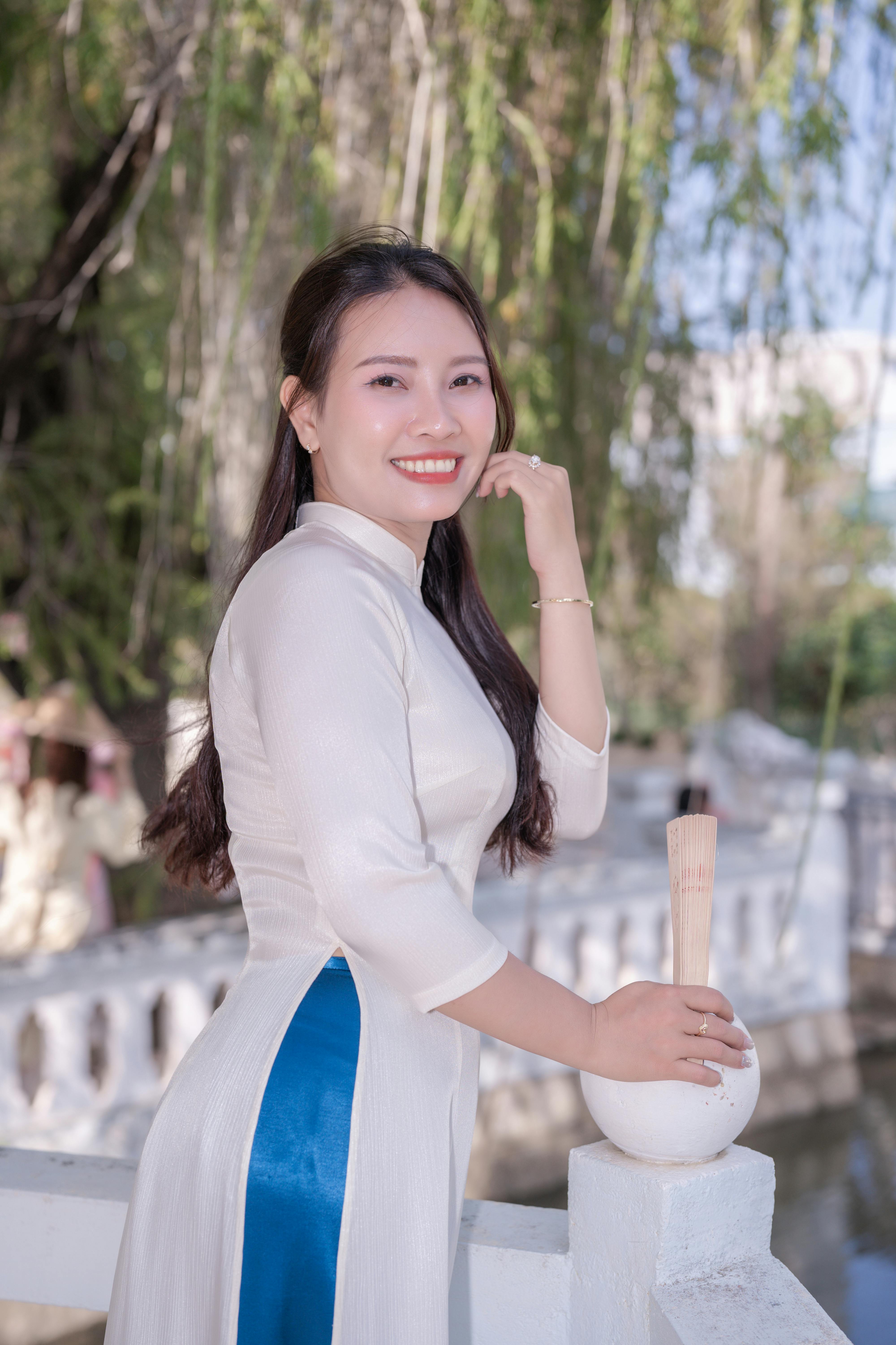 Smiling woman in traditional Vietnamese ao dai standing gracefully by a riverside.