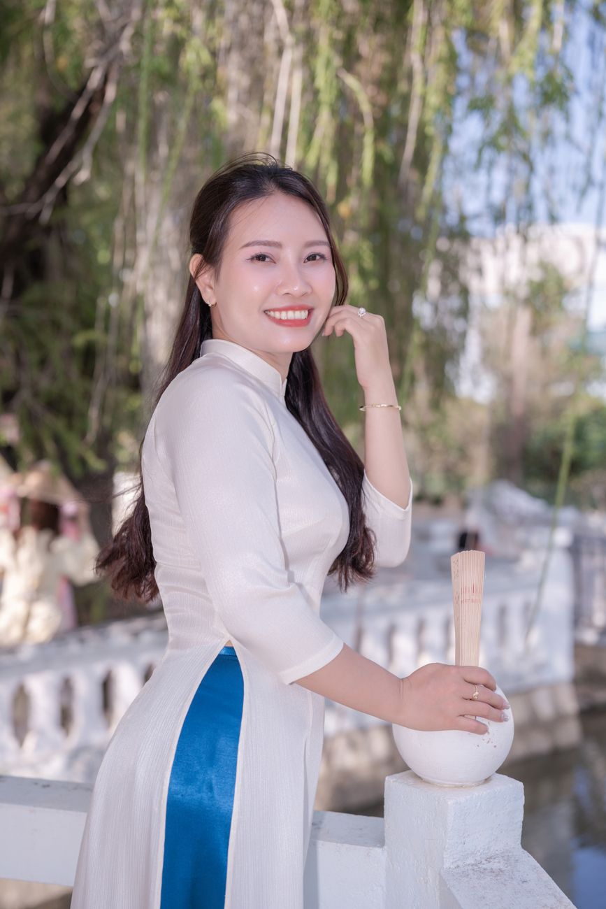 Smiling woman in traditional Vietnamese ao dai standing gracefully by a riverside.