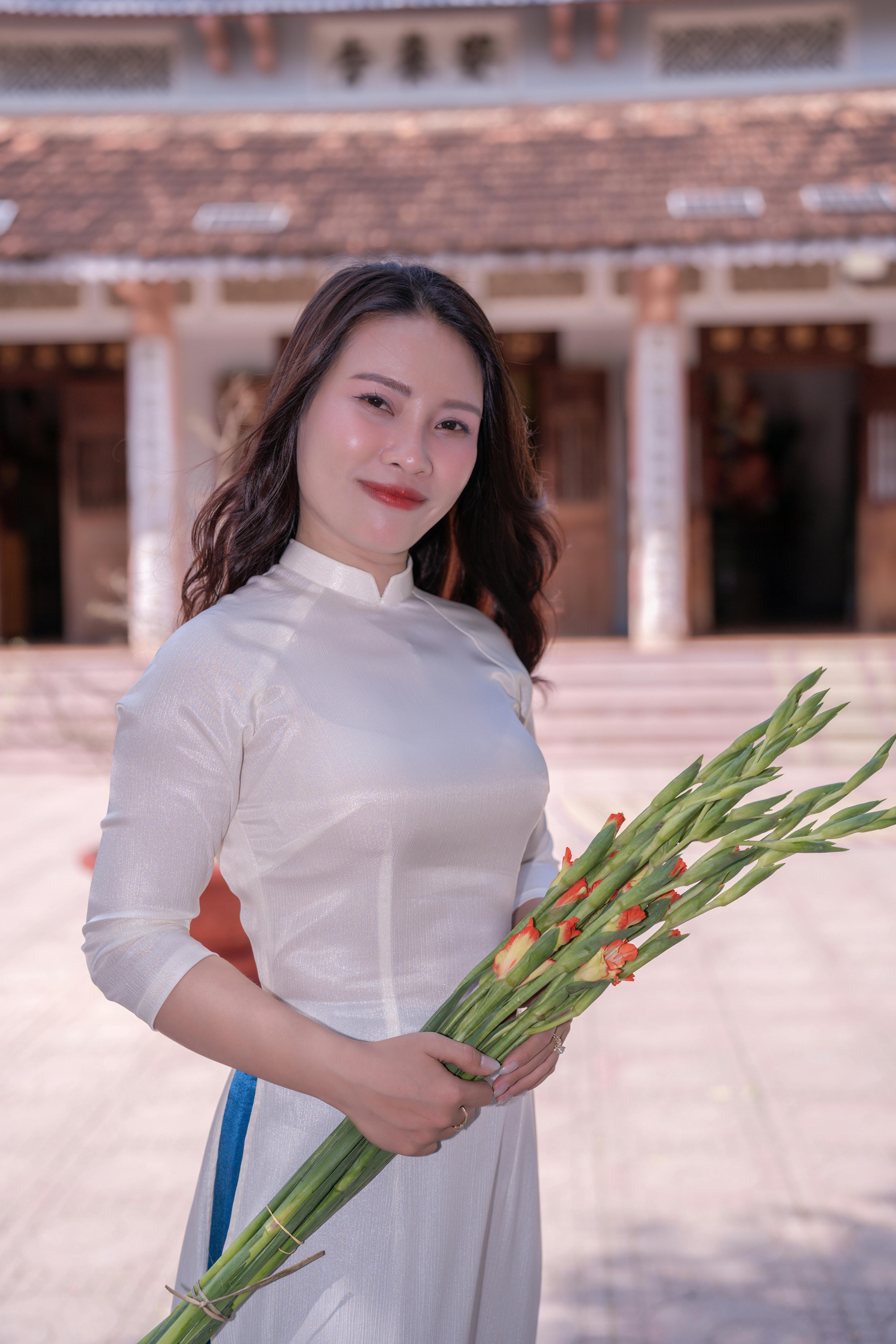 A woman in traditional white dress holding gladiolus flowers outdoors