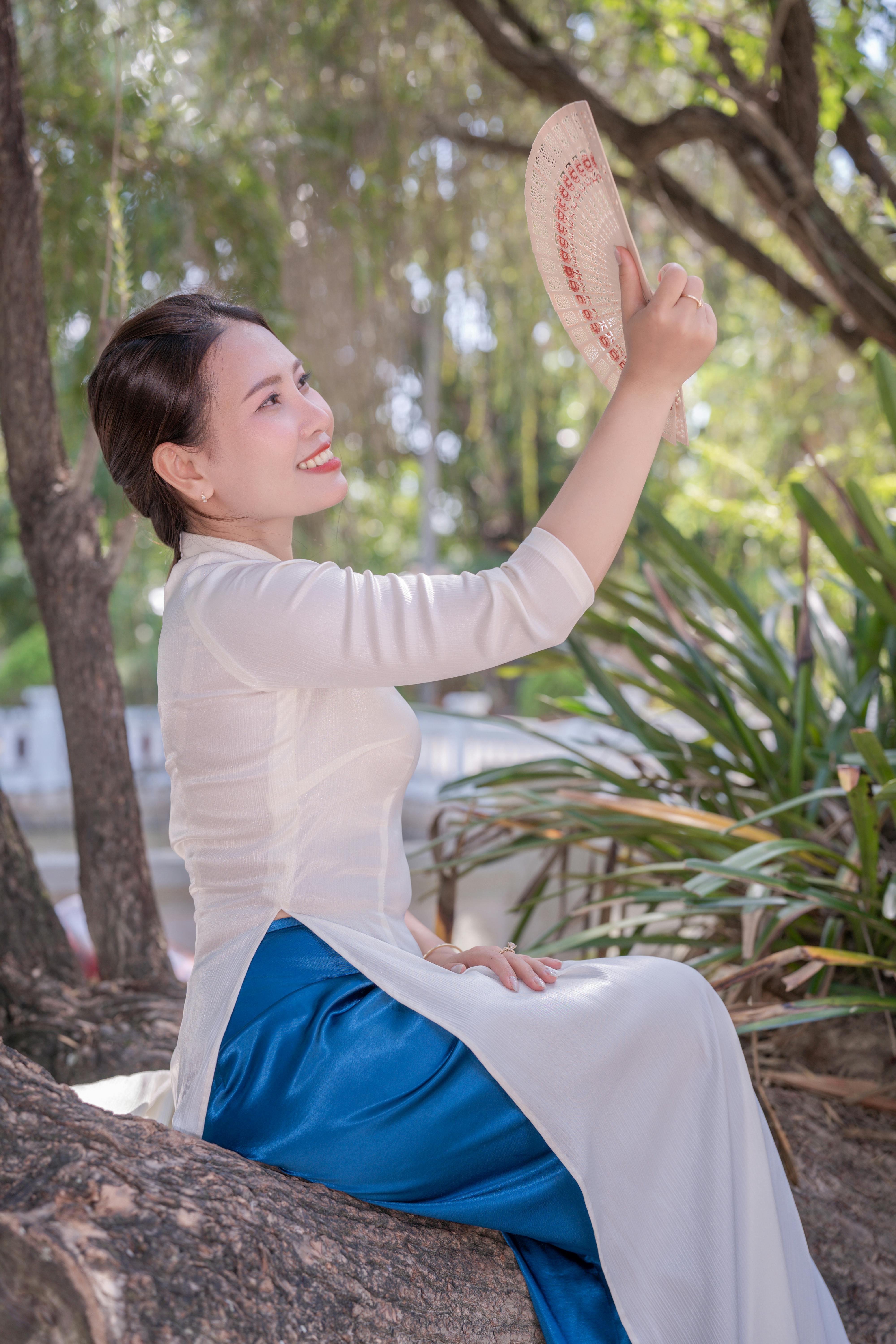 ingyenes Mosolygó nő hagyományos fehér ruhában, legyezőt tartva a szabadban, átölelve a természetet. Stockfotó