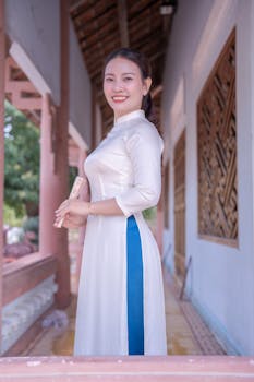 Elegant woman in a traditional white ao dai holding a scroll in an outdoor corridor.