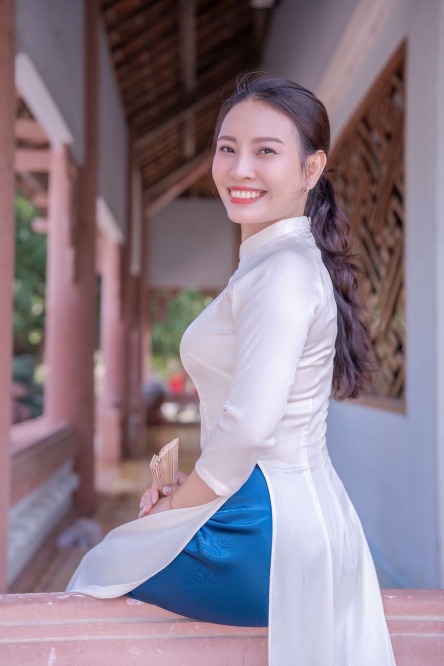 A smiling woman in traditional Vietnamese attire poses outdoors, showcasing cultural beauty.