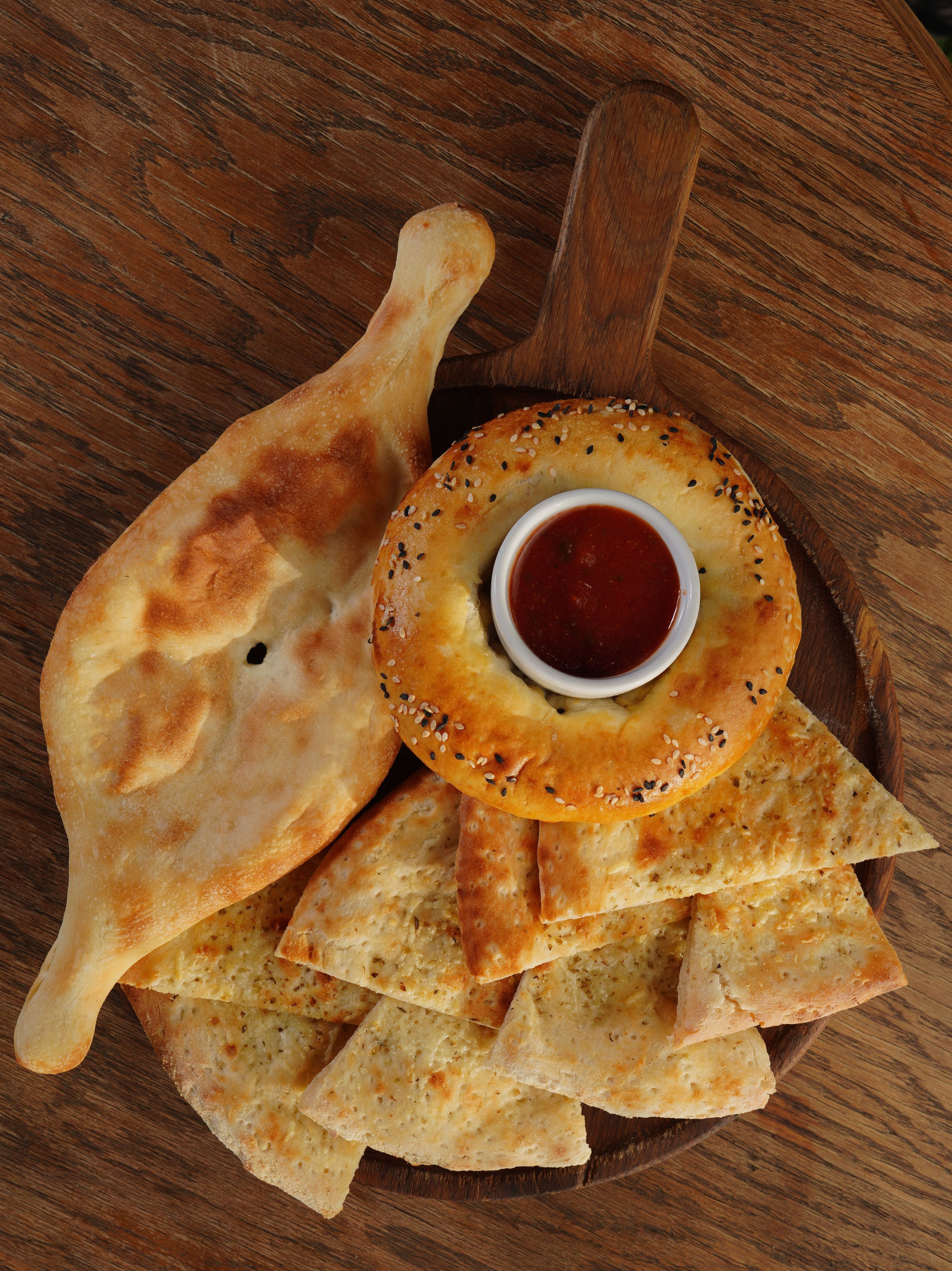 A variety of flatbreads with dipping sauce served on a wooden board, perfect for a rustic meal setting.