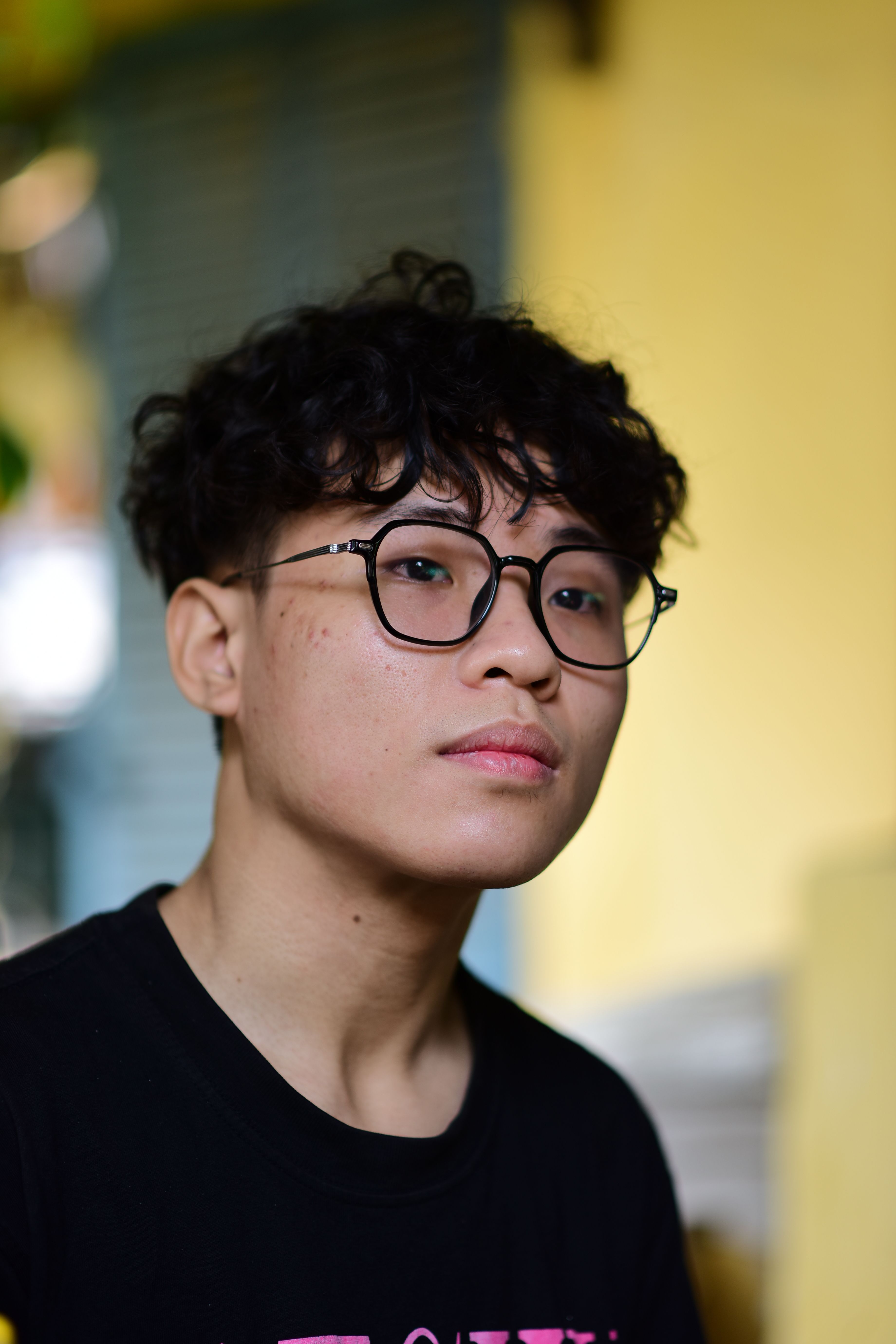 Portrait of a young man with curly hair and glasses, indoors with soft lighting.