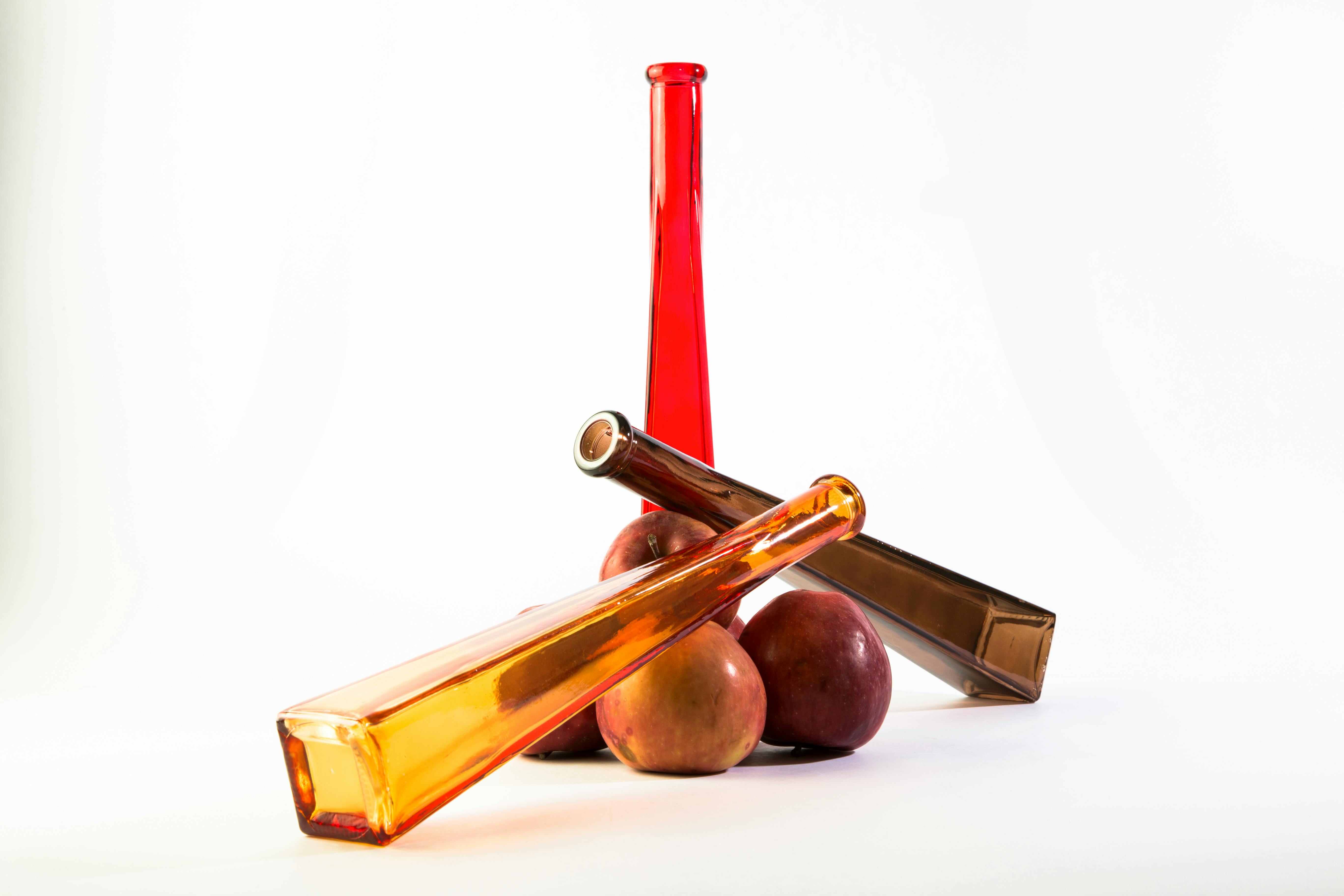 Gratuit Composition artistique de bouteilles en verre colorées et de pommes rouges sur fond blanc. Photos