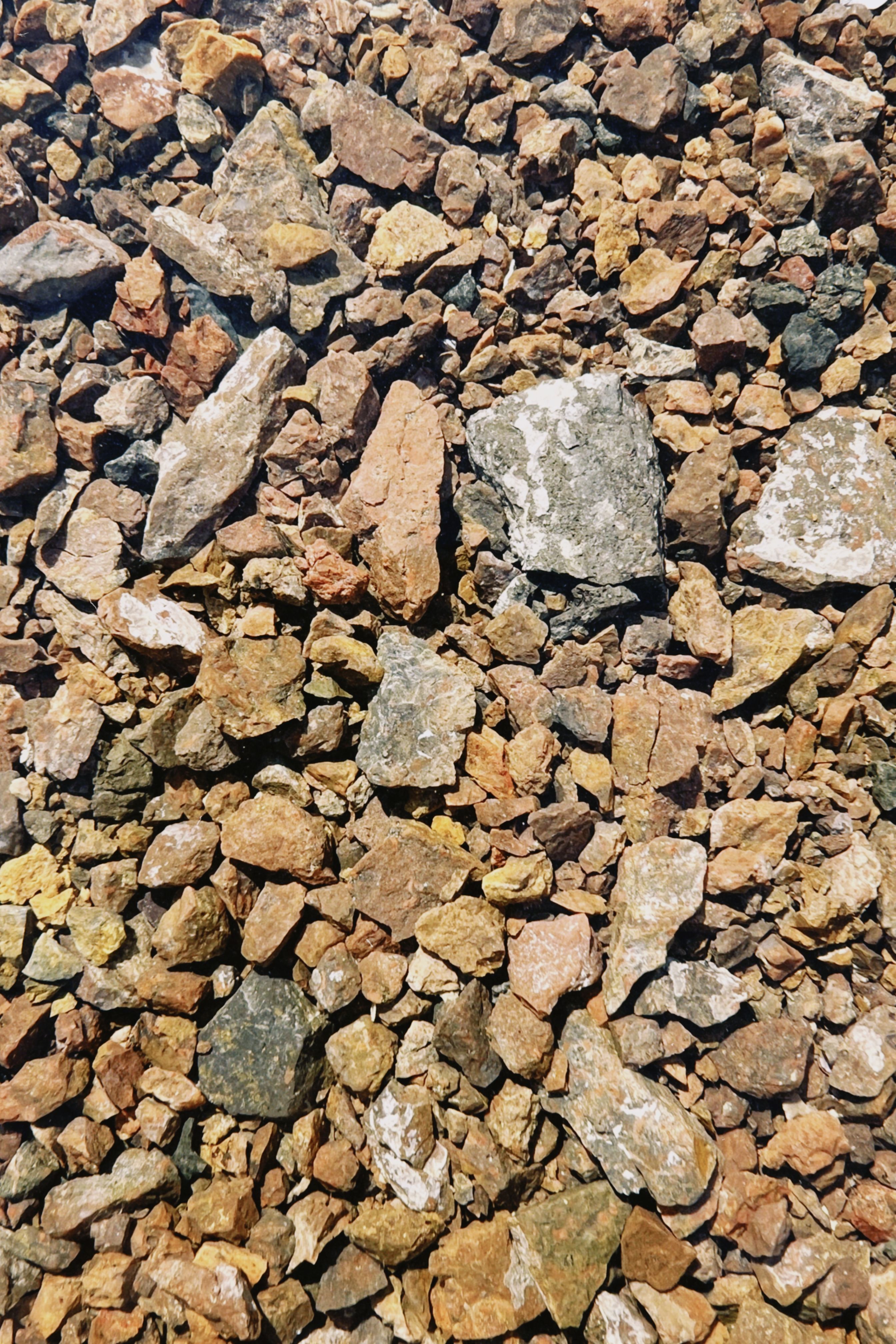 Close-up of a diverse gravel surface showcasing various rock sizes and textures under natural sunlight.