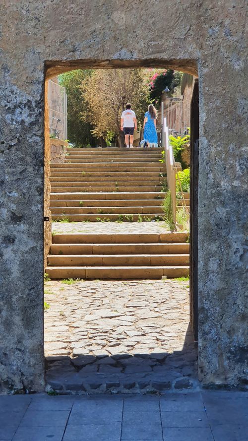 Free View through a stone archway towards steps under summer sun in Alghero, Italy. Stock Photo
