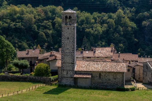 Charming medieval stone bell tower in Camerata Cornello, Lombardy, surrounded by lush greenery.