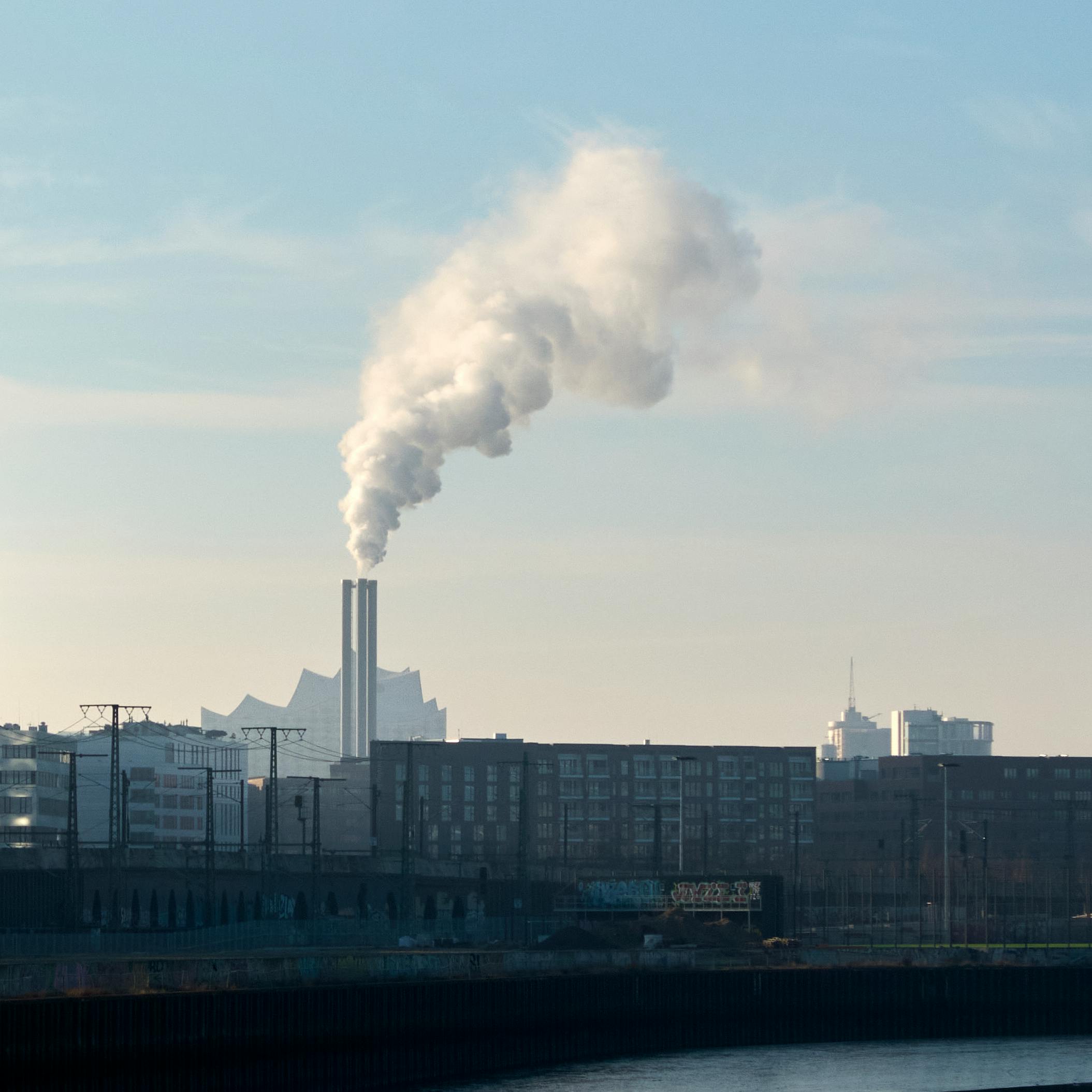 Gratis Røyk velter opp fra en skorstein mot Hamburgs skyline, og fremhever byindustrien. Arkivbilde