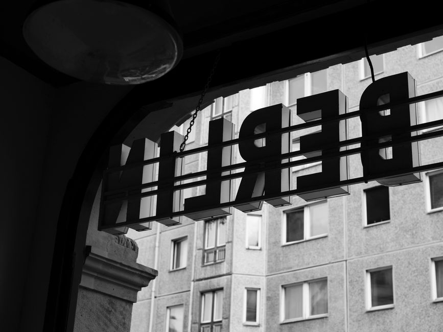 Black and white reflection of a 'BERLIN' sign with urban architecture in the background.