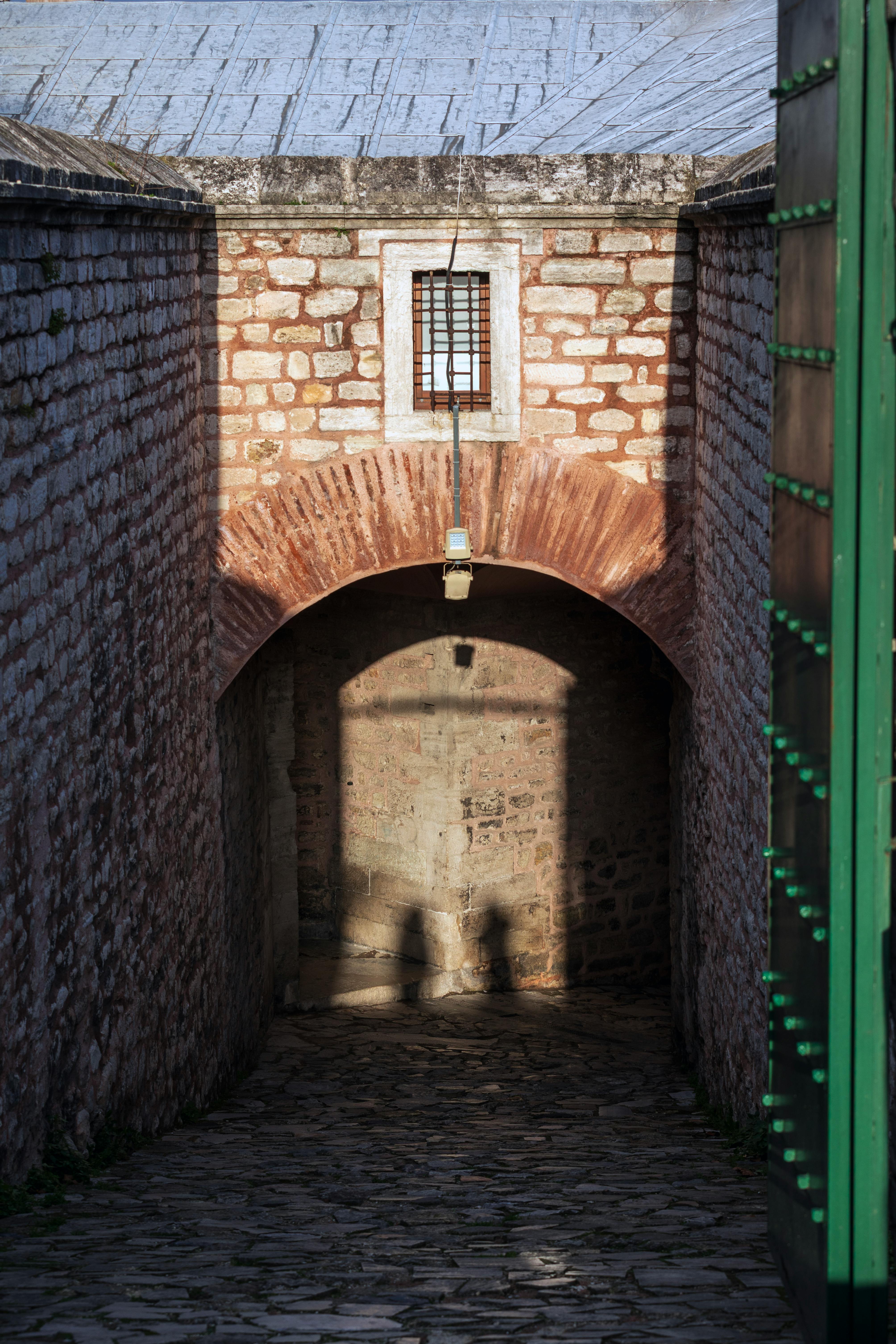 Gratis Sombras en un histórico callejón adoquinado que conduce a un arco de ladrillo bajo la luz del sol. Foto de stock
