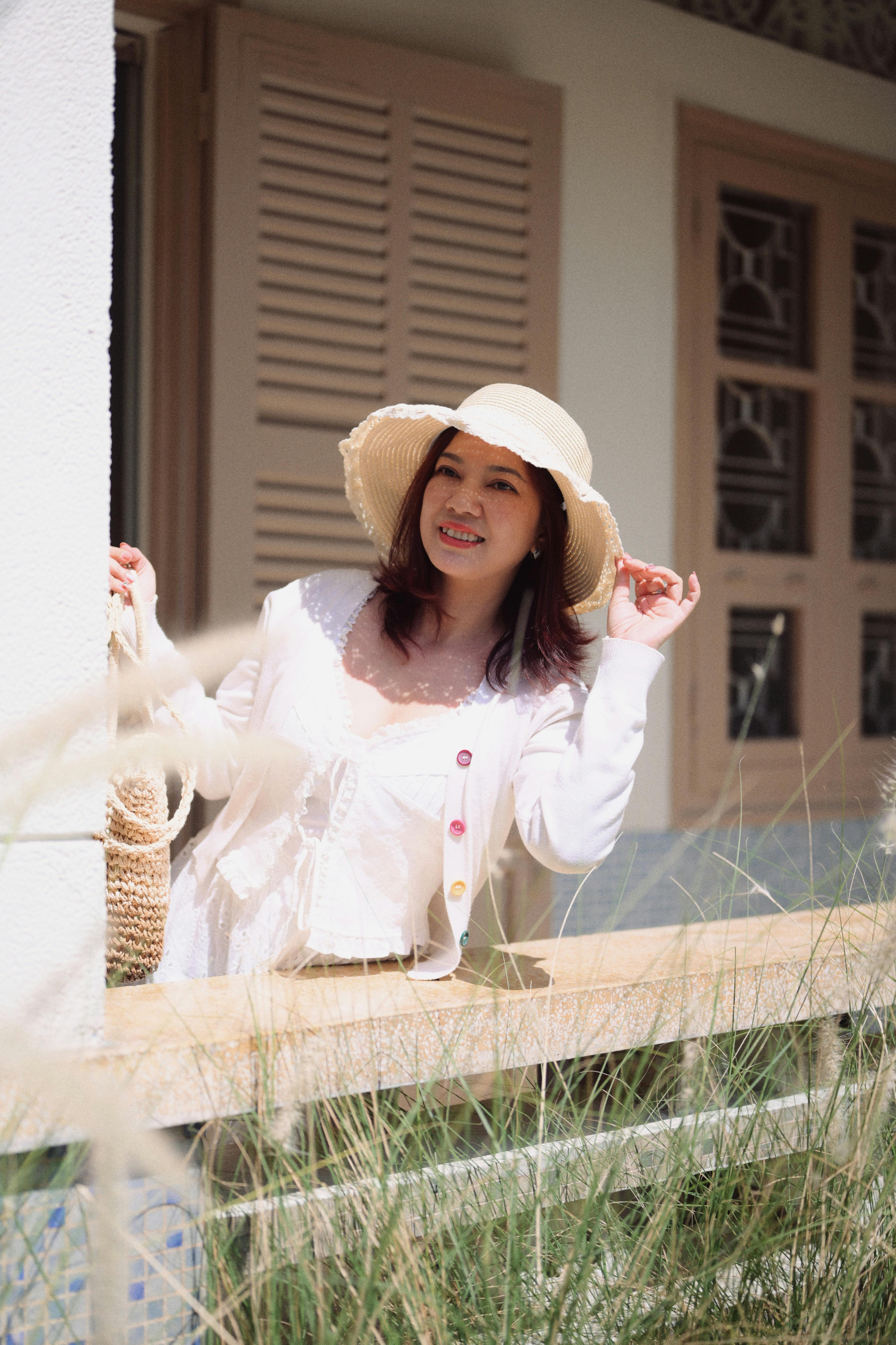 ingyenes Egy vidám nő szalmakalapban élvezi a napsütéses napot a szabadban, a korlátnak támaszkodva. Stockfotó