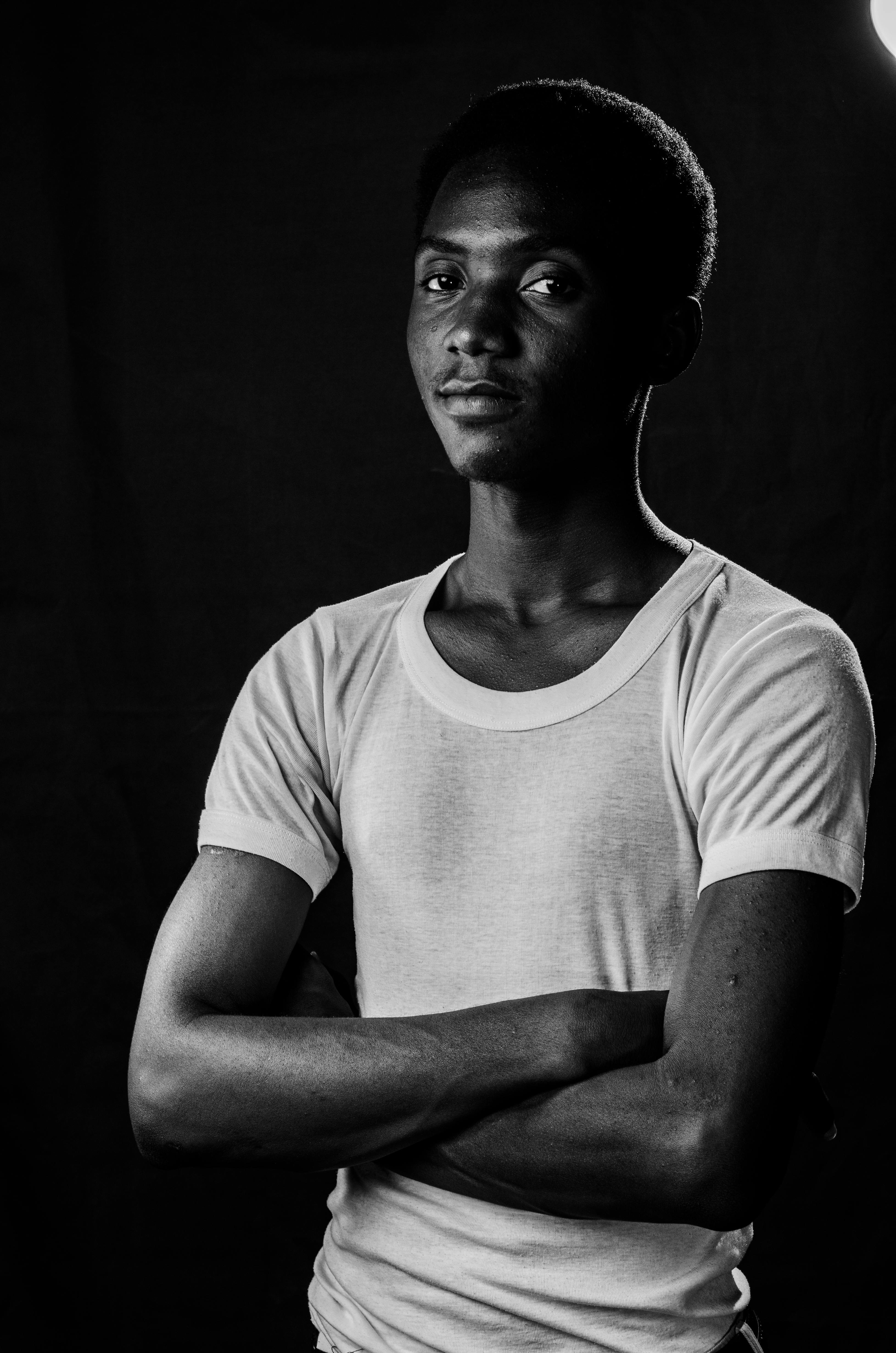 Gratis Un impactante retrato en blanco y negro de un joven de pie con los brazos cruzados. Foto de stock