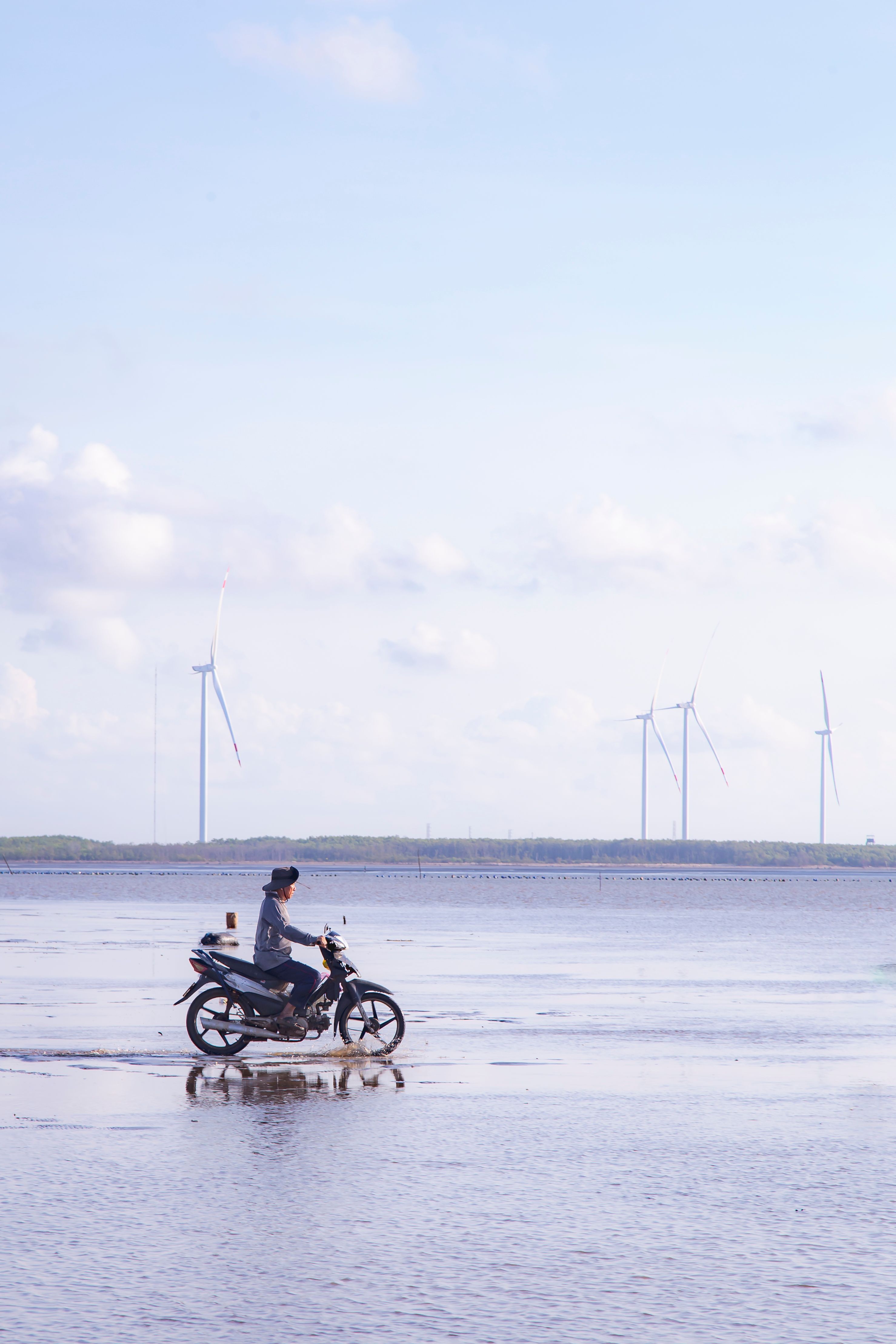 A man rides a motorcycle by wind turbines at the seaside in Bến Tre, Vietnam.