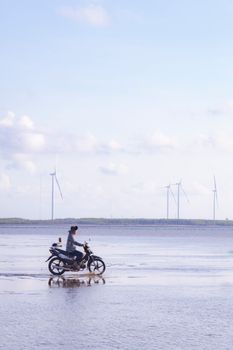 A man rides a motorcycle by wind turbines at the seaside in Bến Tre, Vietnam.