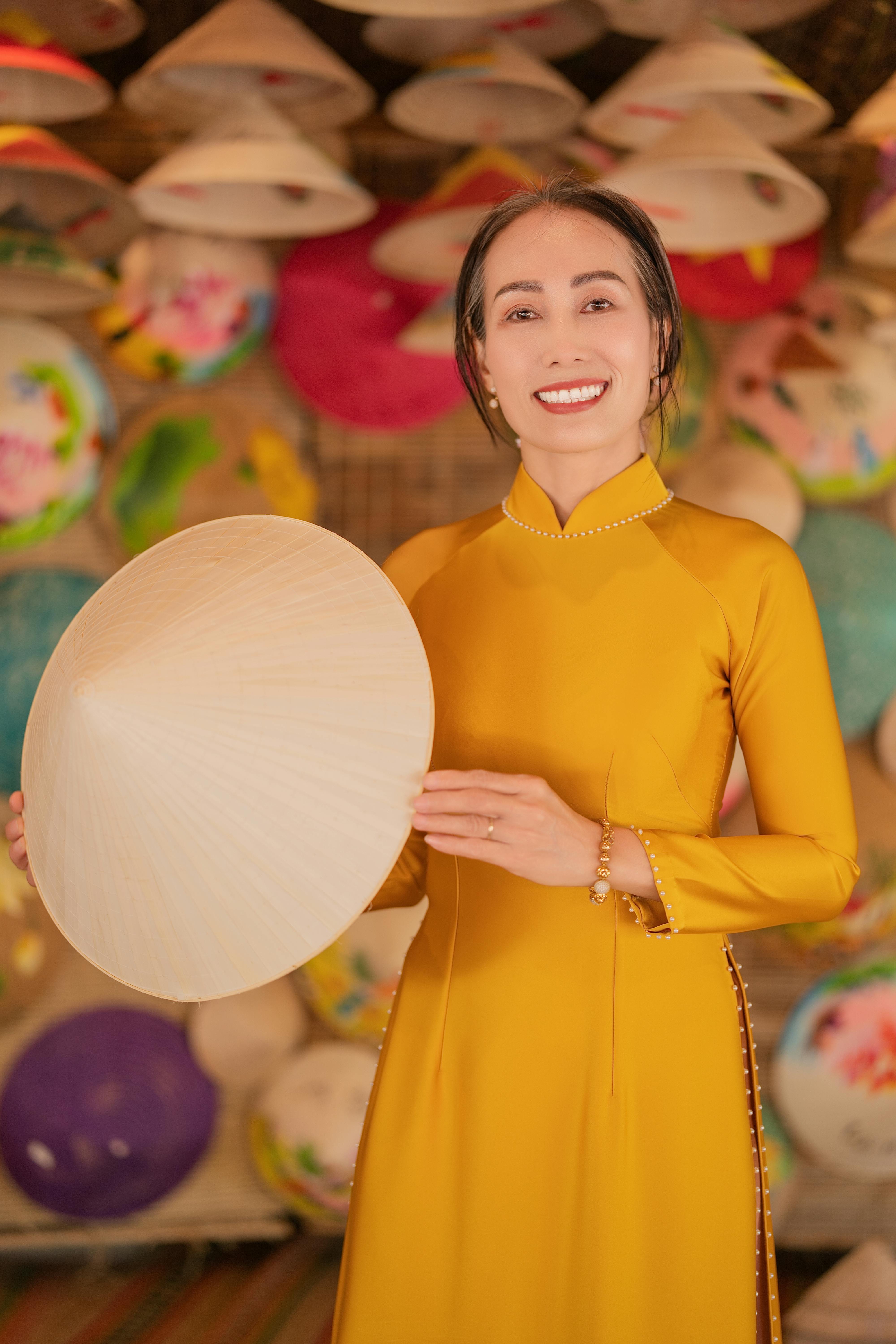 Smiling woman in yellow Ao Dai holding a Non La, surrounded by colorful hats. Vibrant and cultural.