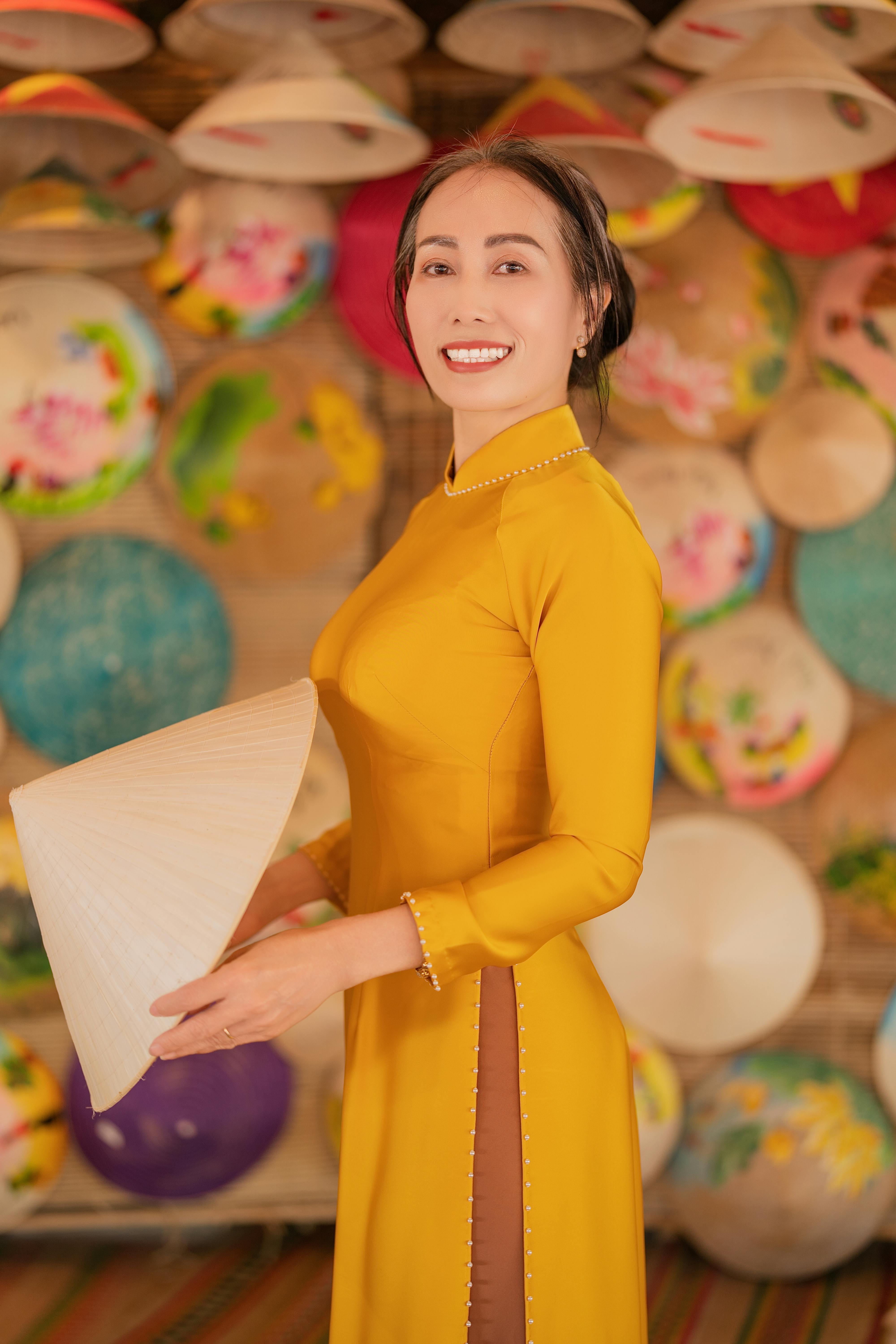 Smiling woman in yellow áo dài with a conical hat, showcasing Vietnamese culture.
