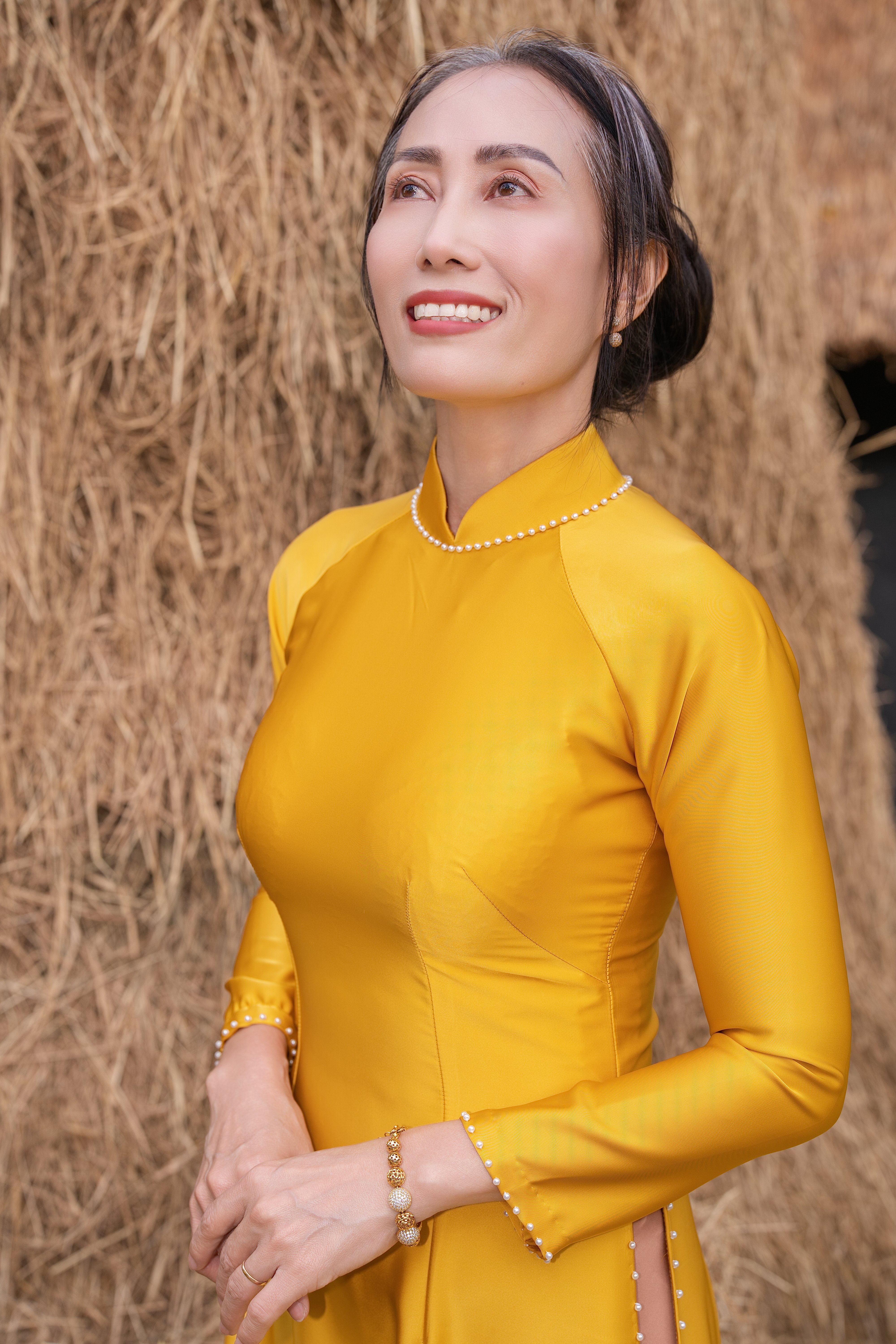 Smiling woman in a yellow ao dai stands by straw hay. Bright and elegant portrait.