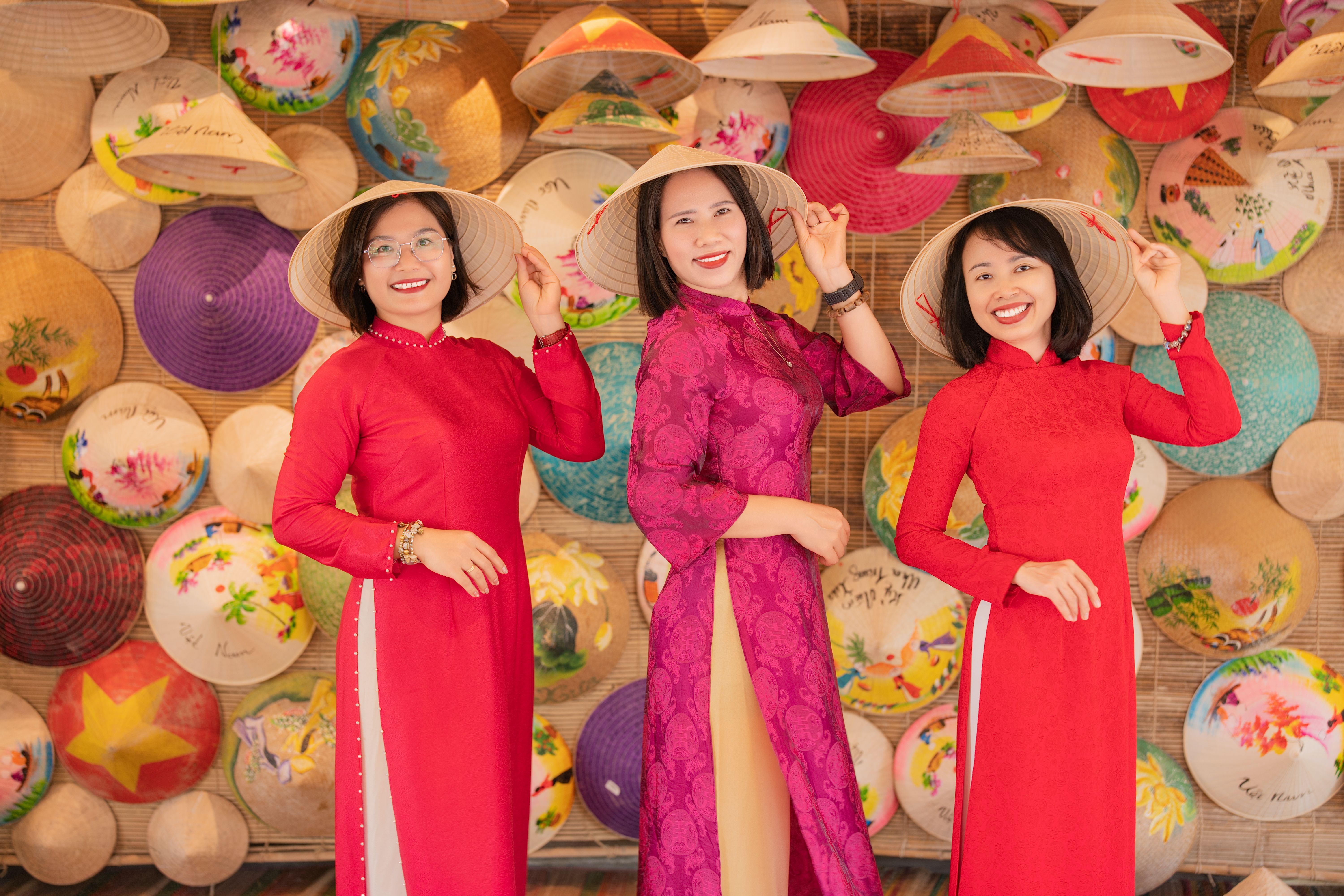 Three women wearing traditional dresses and conical hats posing indoors.