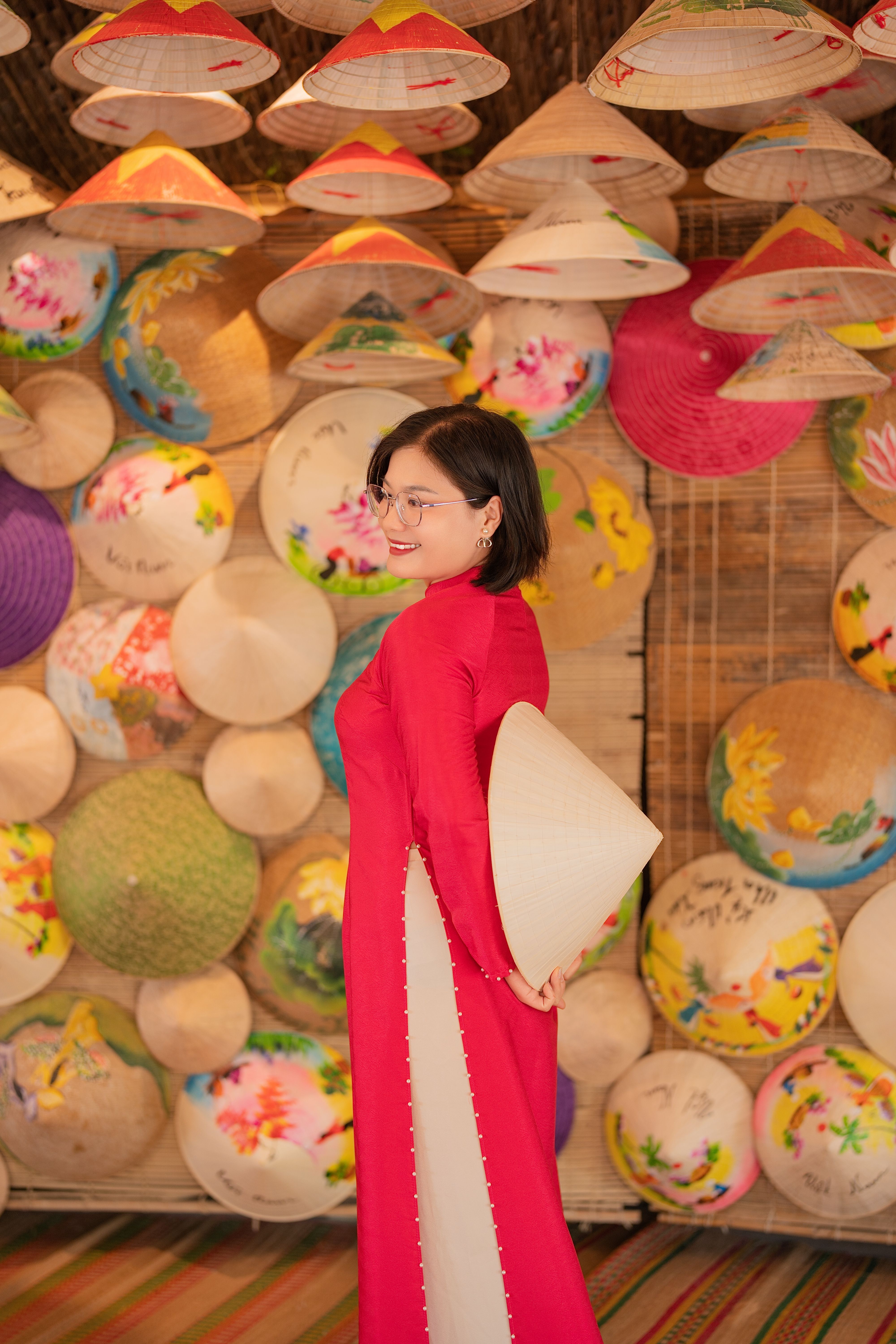 Woman wearing red Ao Dai holds conical hat in culturally vibrant setting.
