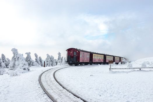 A red train travels through a snowy landscape in Saxony-Anhalt during winter.