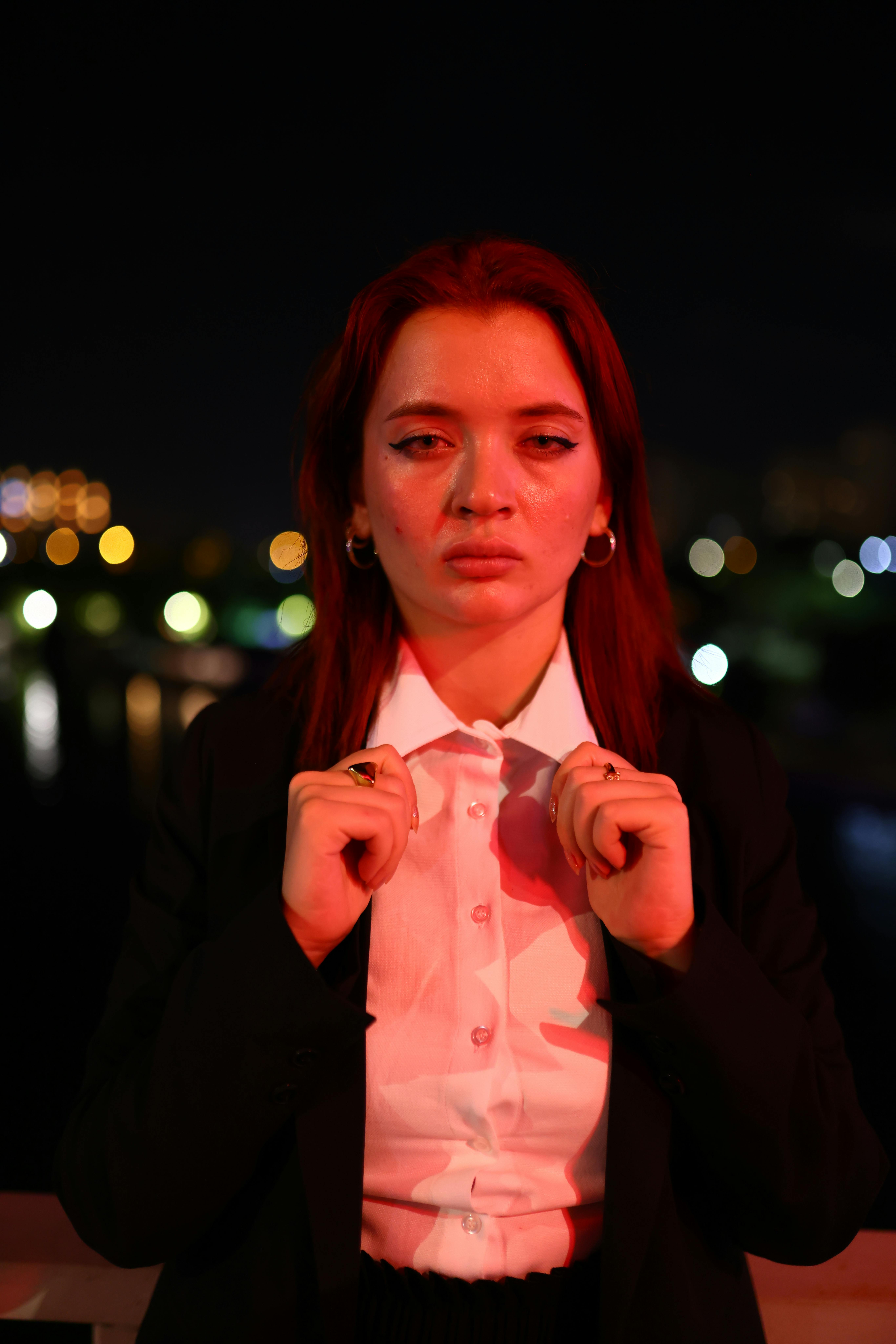 grátis Uma mulher vestida formalmente está em pé ao ar livre à noite, com luzes da cidade desfocadas ao fundo. Foto profissional