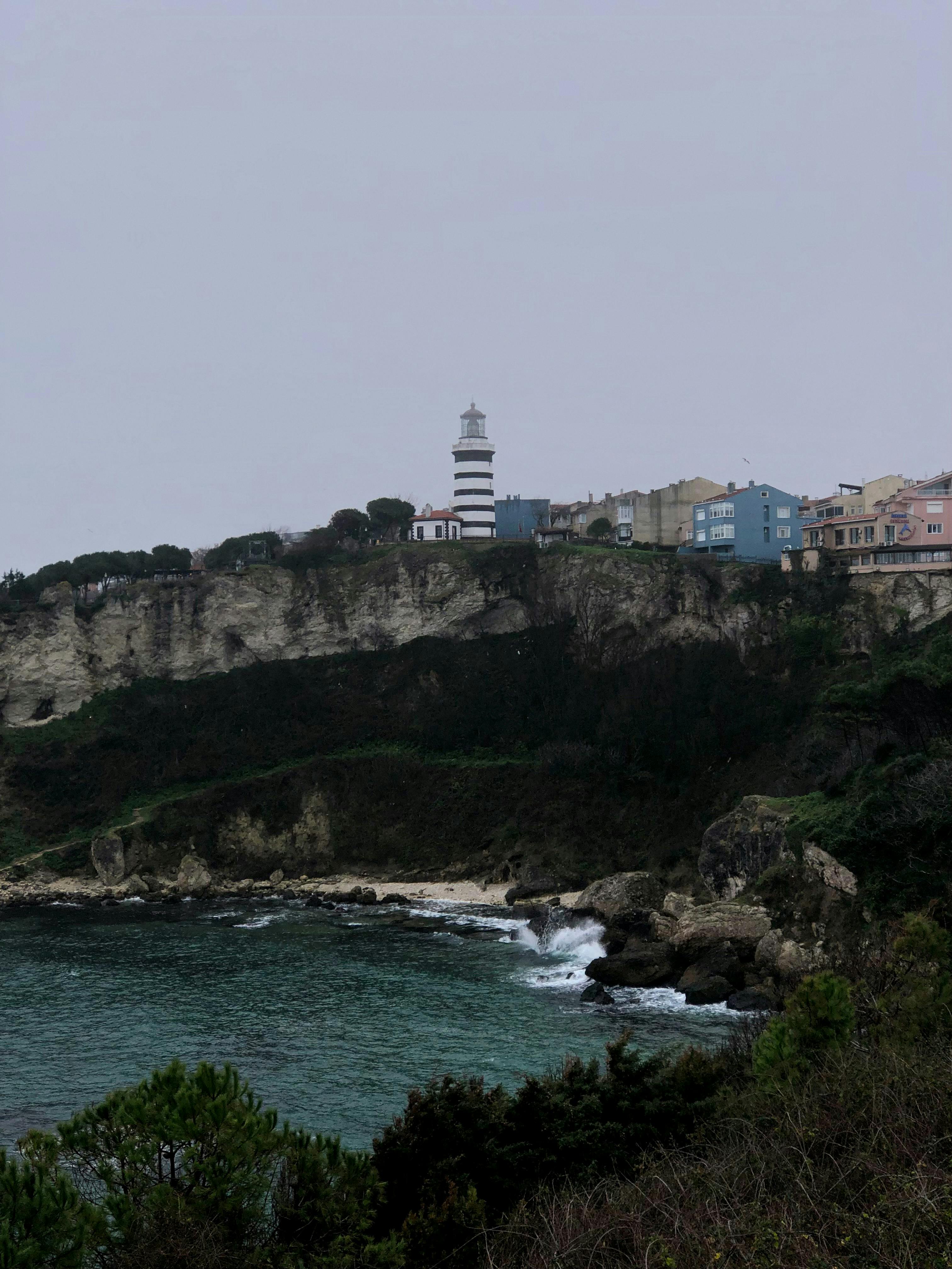 Gratis Et pittoresk fyrtårn som ligger på en klippe over en steinete kystlinje, under en overskyet himmel. Arkivbilde