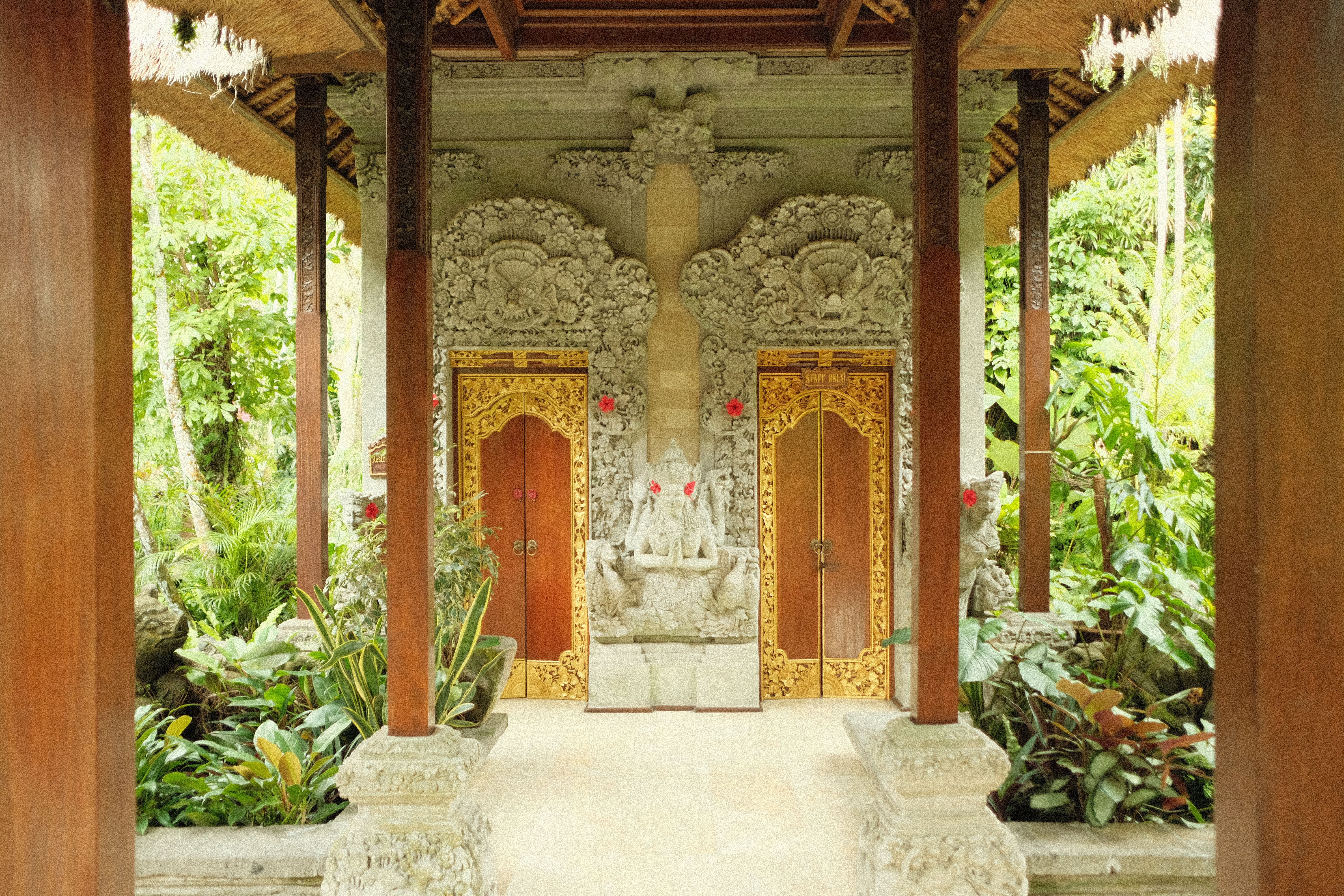 Carved wooden doors inside an open Balinese pavilion surrounded by plants. Illustrative photo