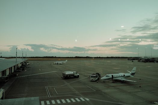 View of private jets and service vehicles on an airport tarmac during dawn light.