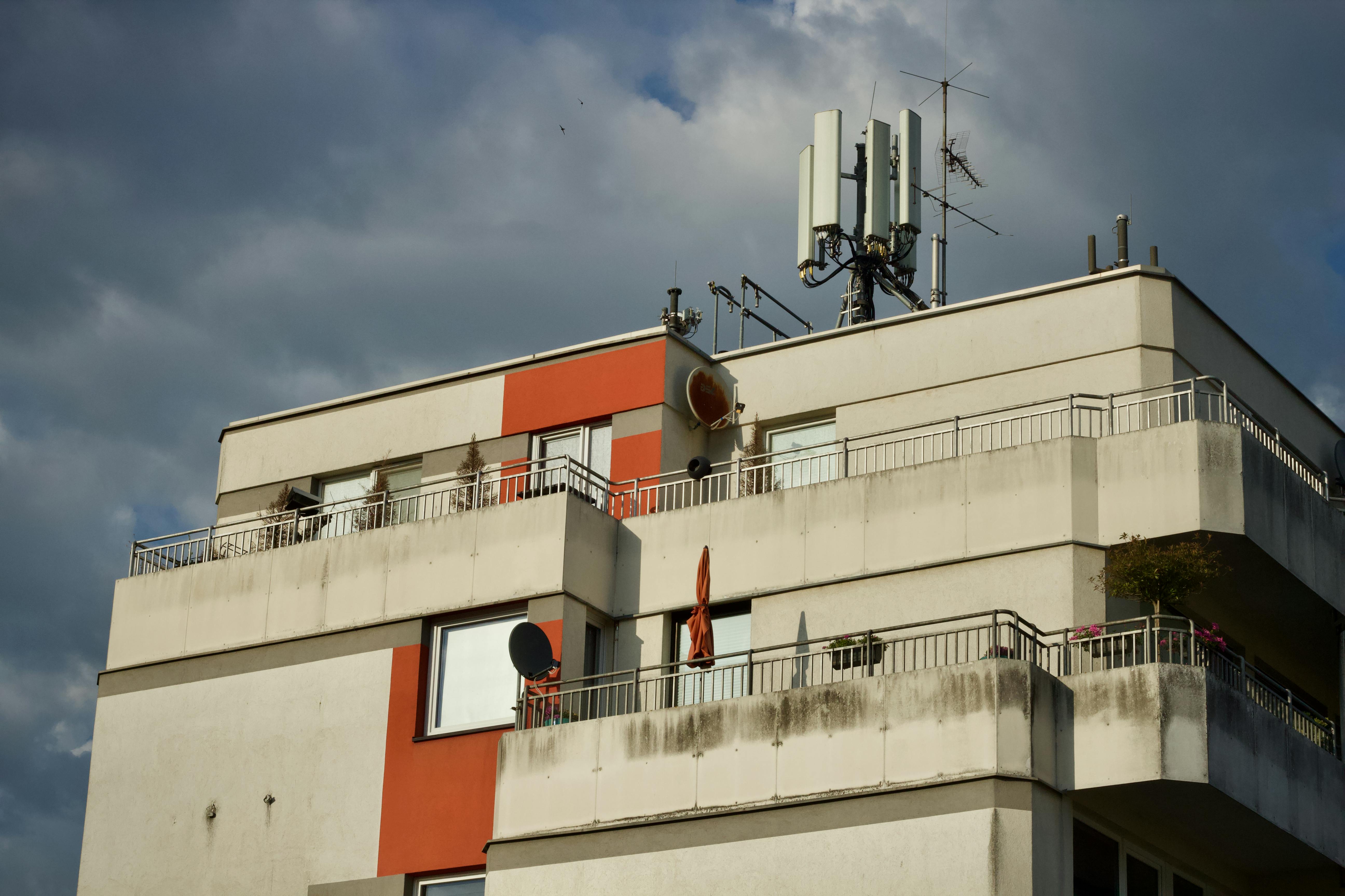 Photo of a modern apartment building with a rooftop antenna under a cloudy sky.