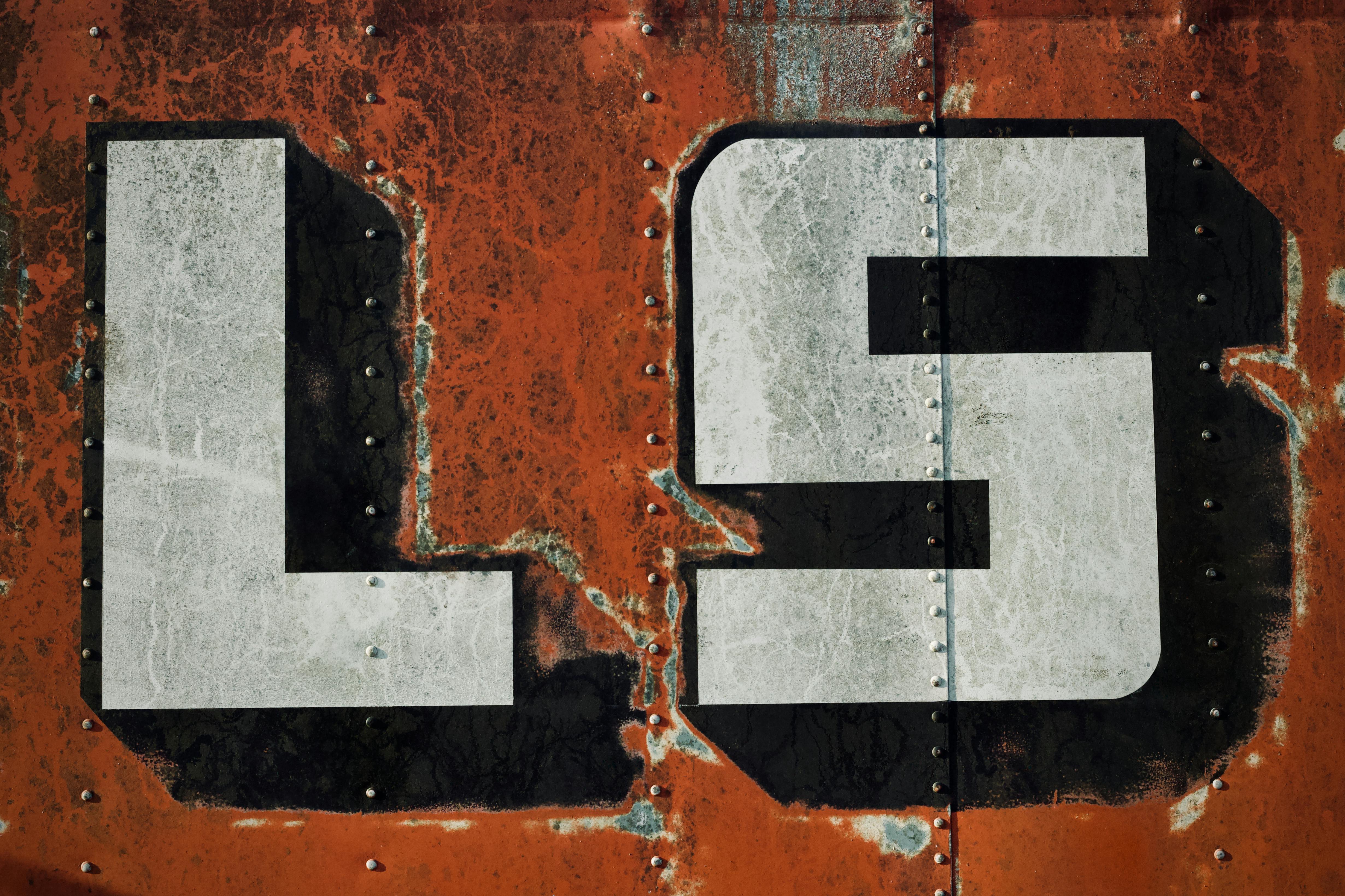 Free Close-up of weathered orange metal with bold white letters 'LS', showcasing texture. Stock Photo