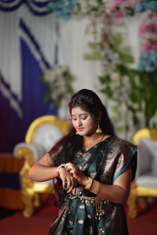 Free A woman in traditional attire adjusting her bracelet during a ceremonial event indoors. Stock Photo