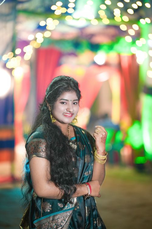 Free A smiling Indian woman dressed in traditional attire celebrates under festive lights, showcasing cultural elegance. Stock Photo