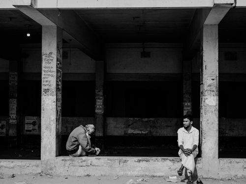 Free A black and white street photograph featuring two men seated in an urban setting, conveying solitude. Stock Photo
