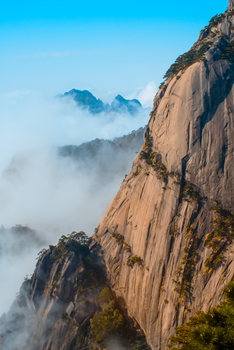 Scenic view of rocky mountain peaks shrouded in mist with a vibrant blue sky.