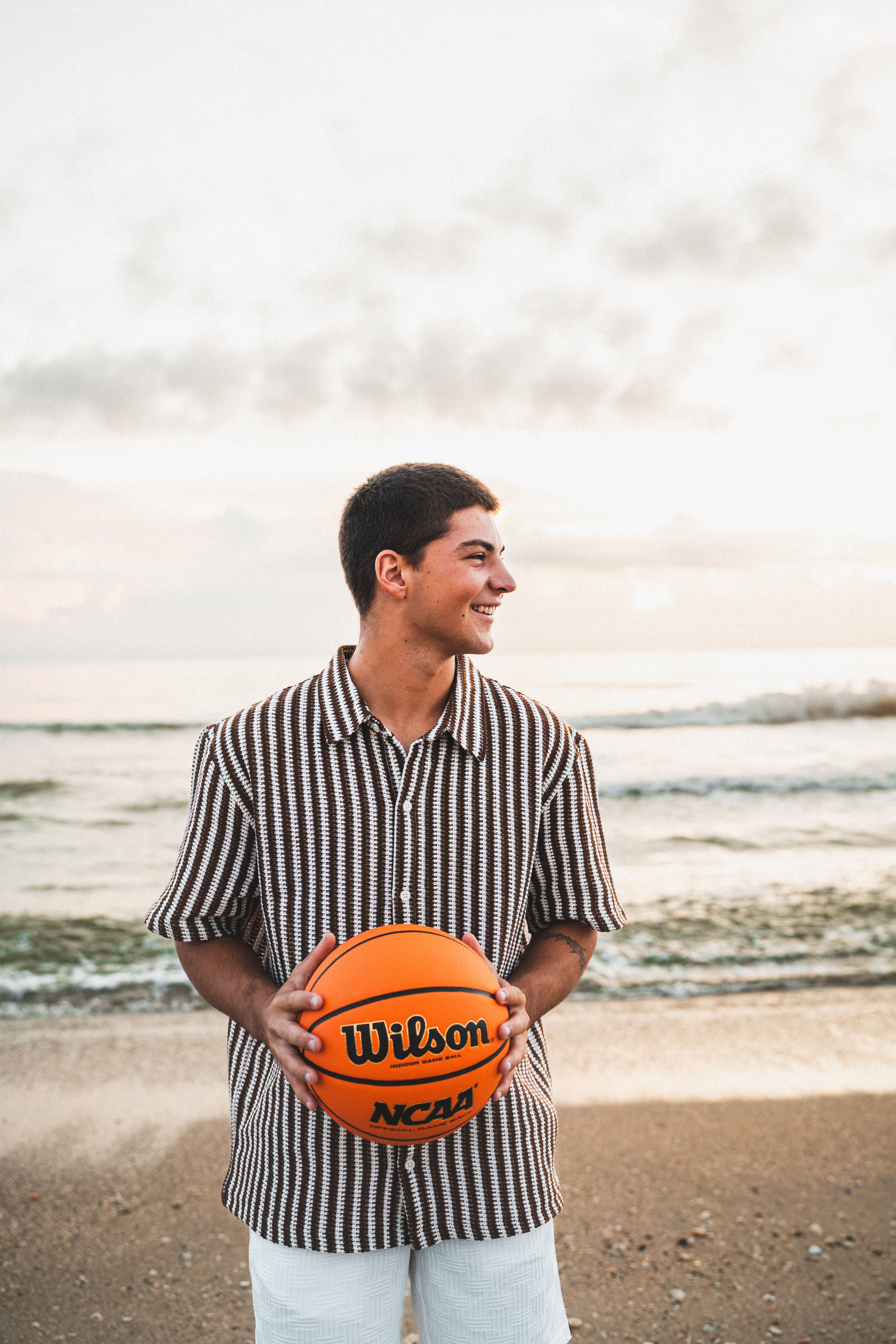 A young man holding a basketball stands on Melbourne Beach during sunset.