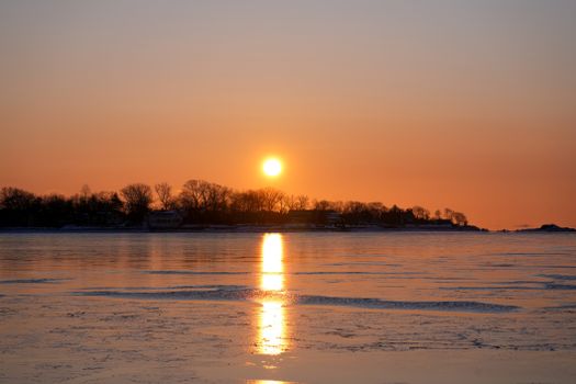 A tranquil winter sunset reflected on a frozen lake with silhouetted trees.