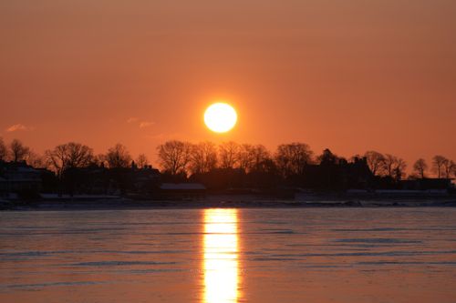 Free Stunning sunset over a frozen lake with silhouetted trees reflecting warm tones on ice. Stock Photo
