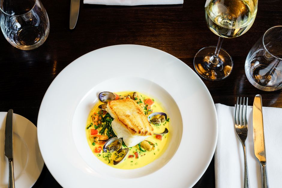 Exquisite seafood dish with clams and fish served at an elegant London restaurant, paired with white wine.
