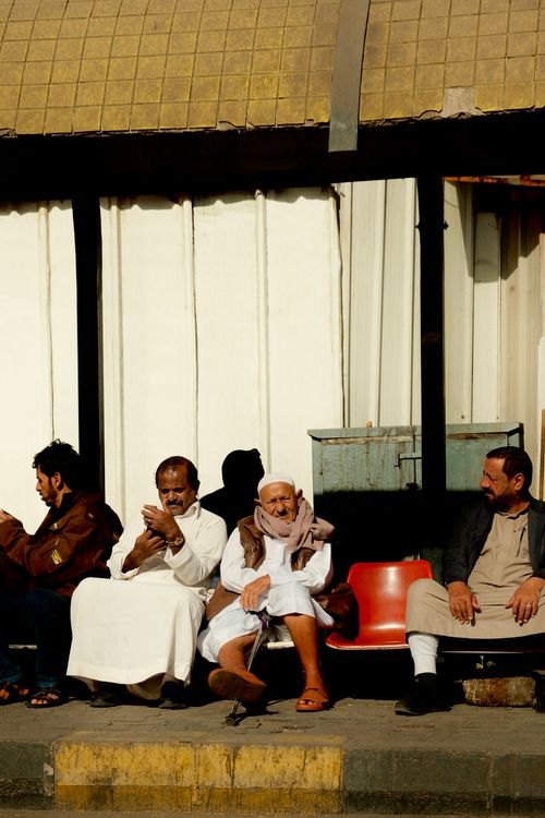 Free A group of men relaxing at a bus stop in bright daylight, capturing daily life. Stock Photo