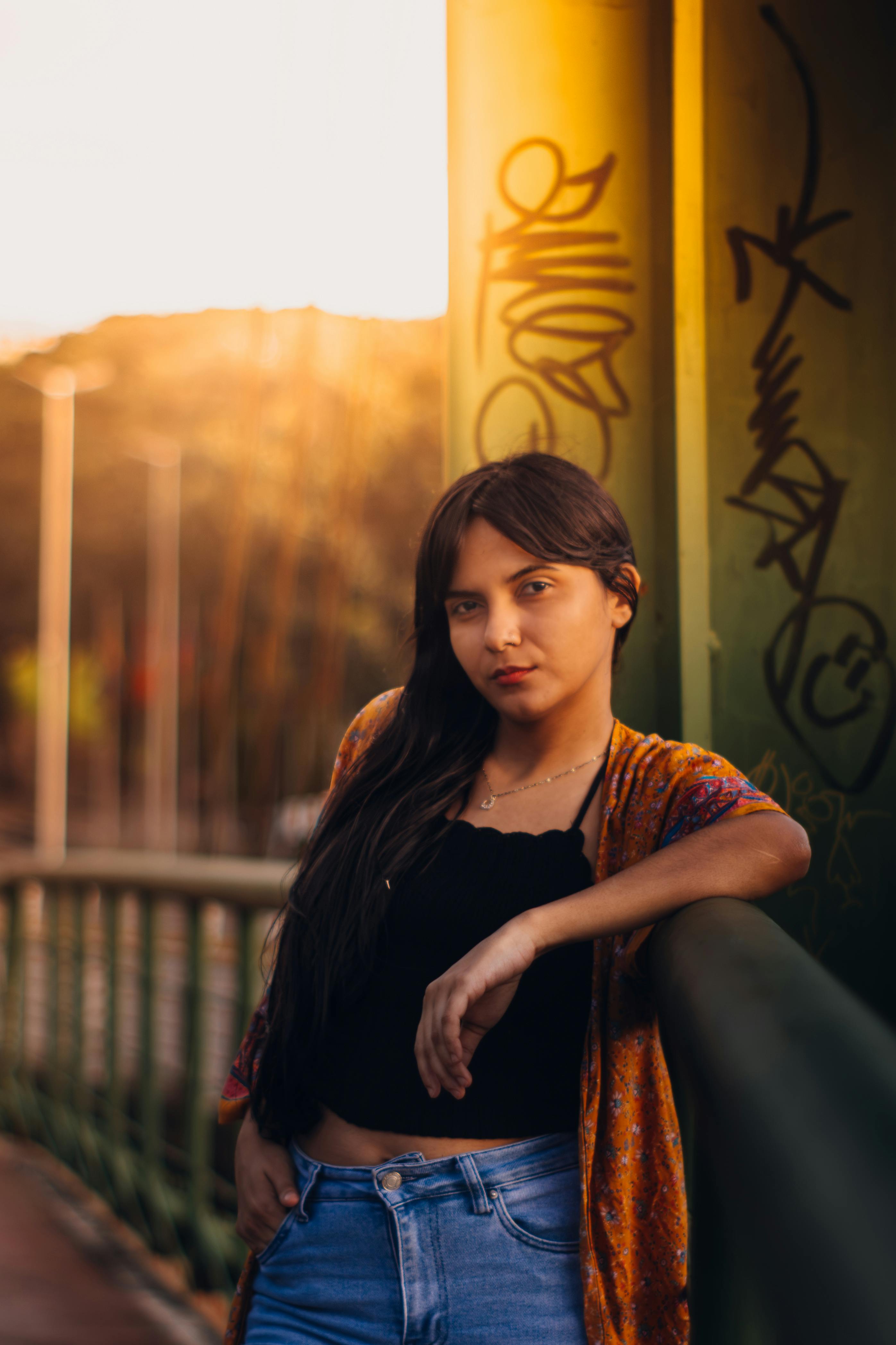 Free Young woman poses casually on an urban bridge at sunset, showcasing street style and vibrant art. Stock Photo