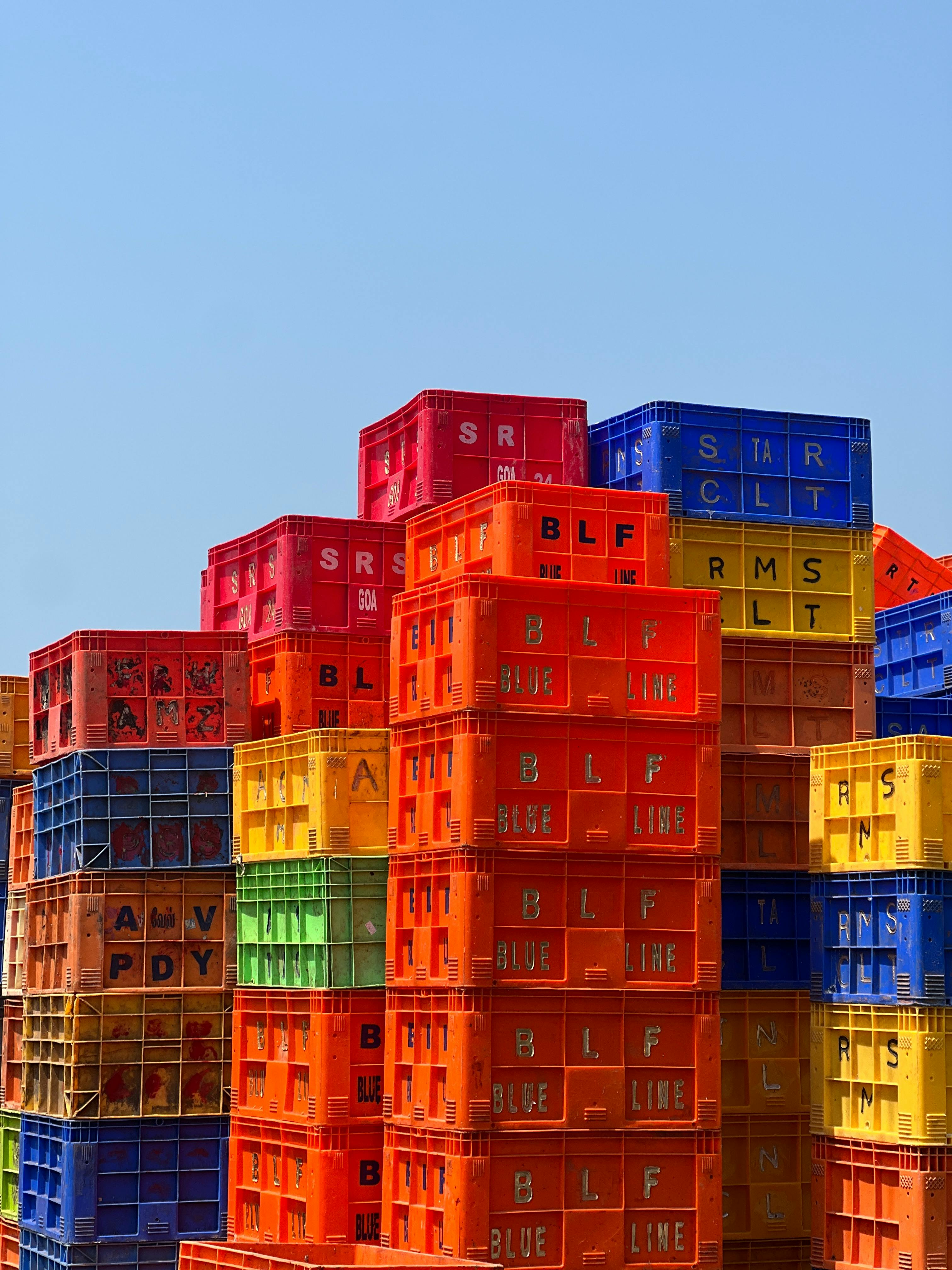 Gratis Fargerike plastkasser stablet høyt under en klar blå himmel, og danner et levende mønster. Arkivbilde