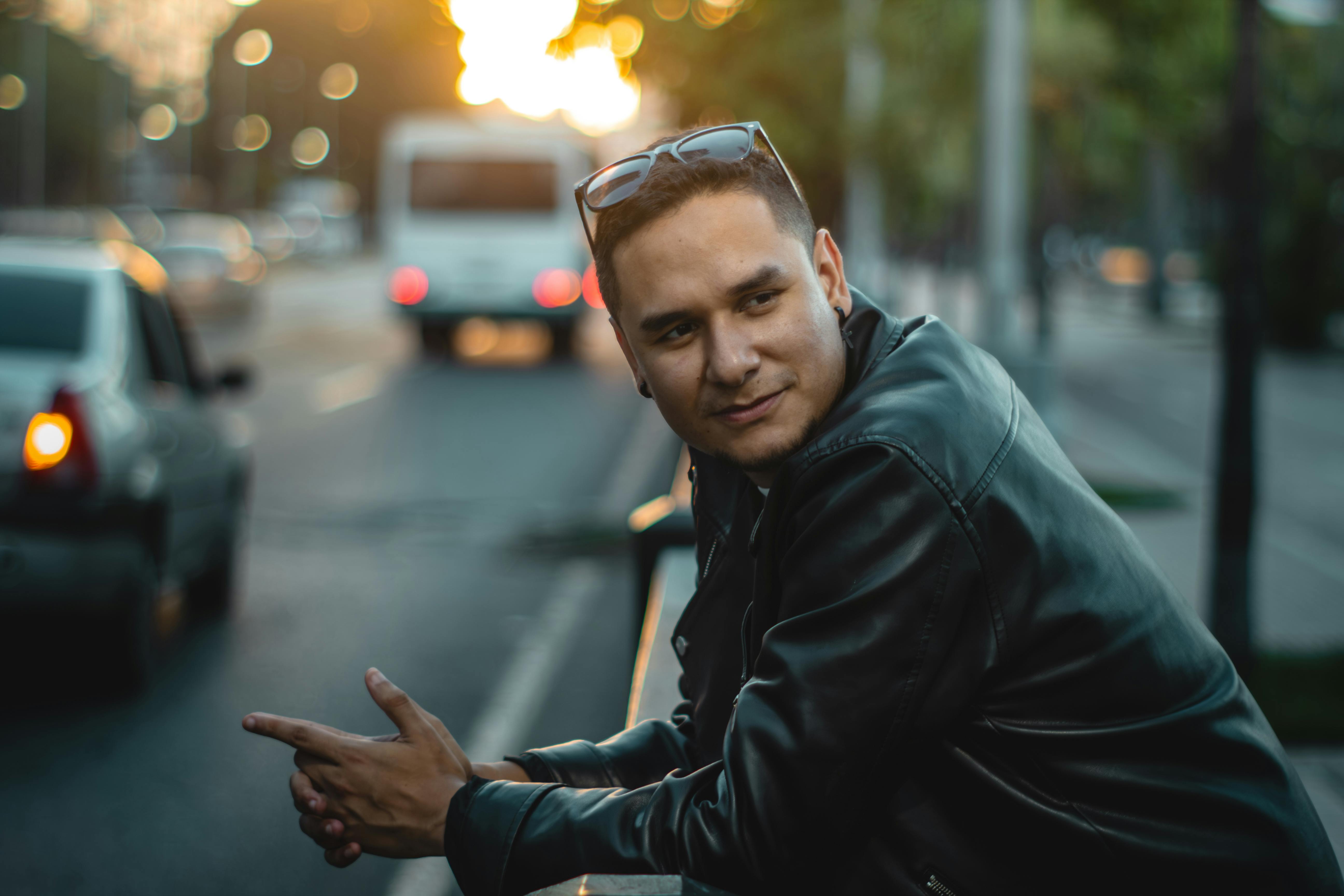 gratis Jonge man in leren jas leunt tegen een reling in de stad bij zonsondergang. Stockfoto