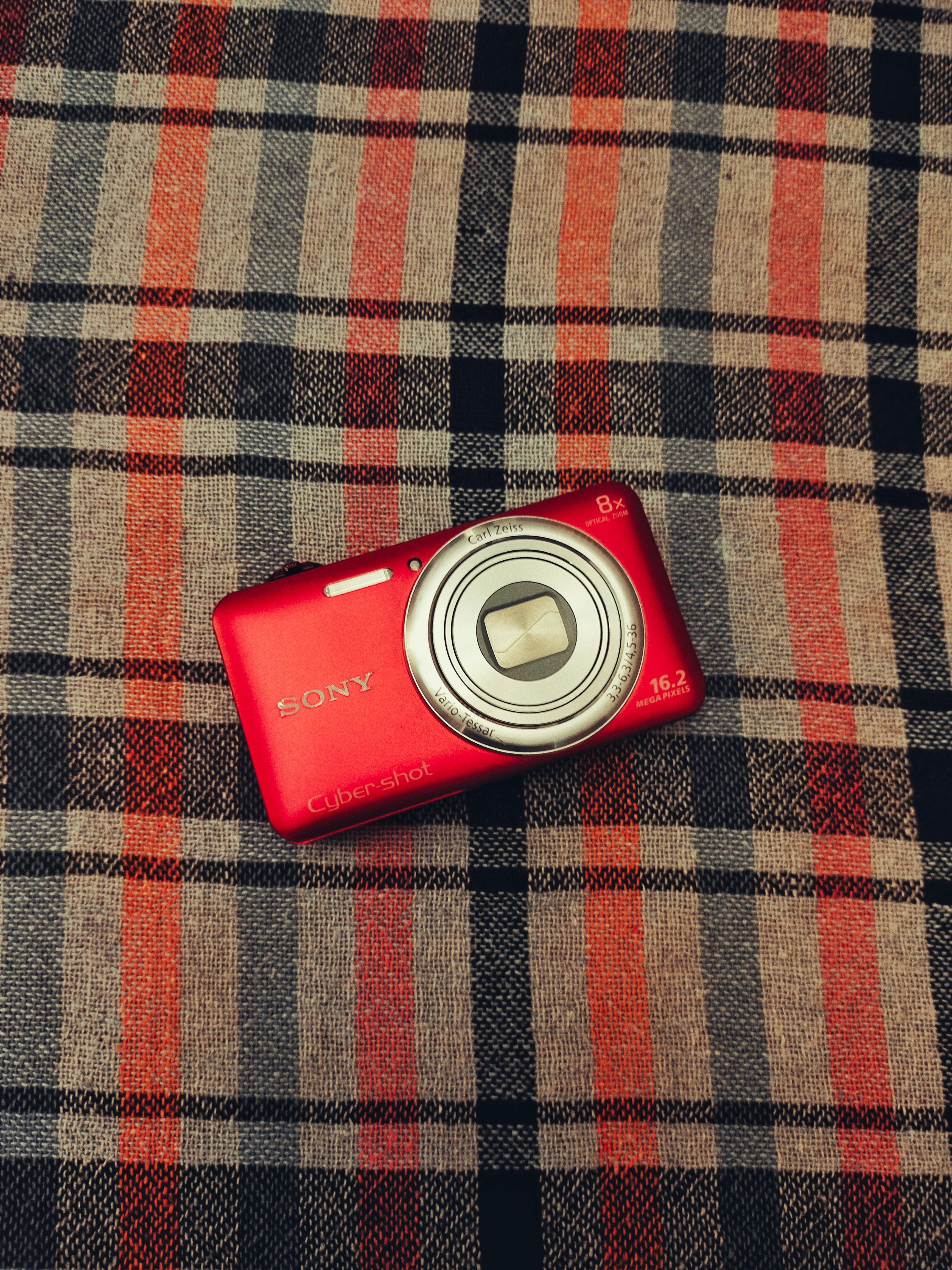 Kostenlos Eine leuchtend rote Kompaktkamera auf kariertem Stoff. Perfekt für Retro-Themen. Stock-Foto